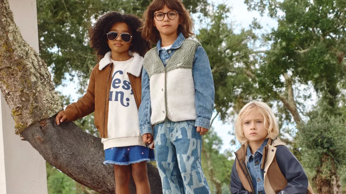 Children in stylish autumn outfits stand on a modern concrete structure amidst a serene forest landscape.
