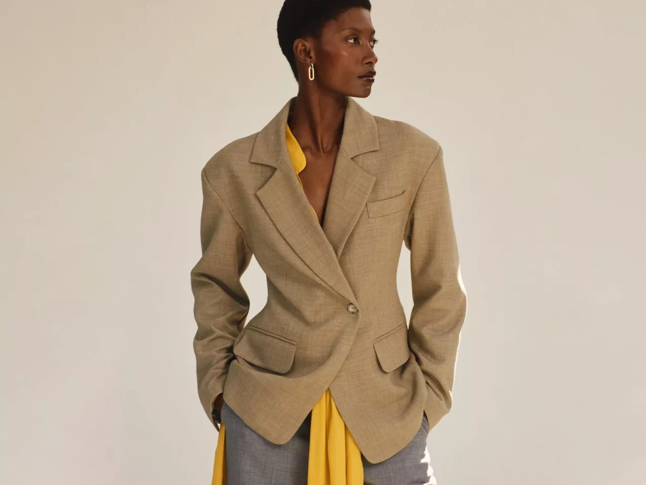 A stylish outfit featuring a beige blazer, yellow shirt, and grey trousers. Elegant and modern fashion.