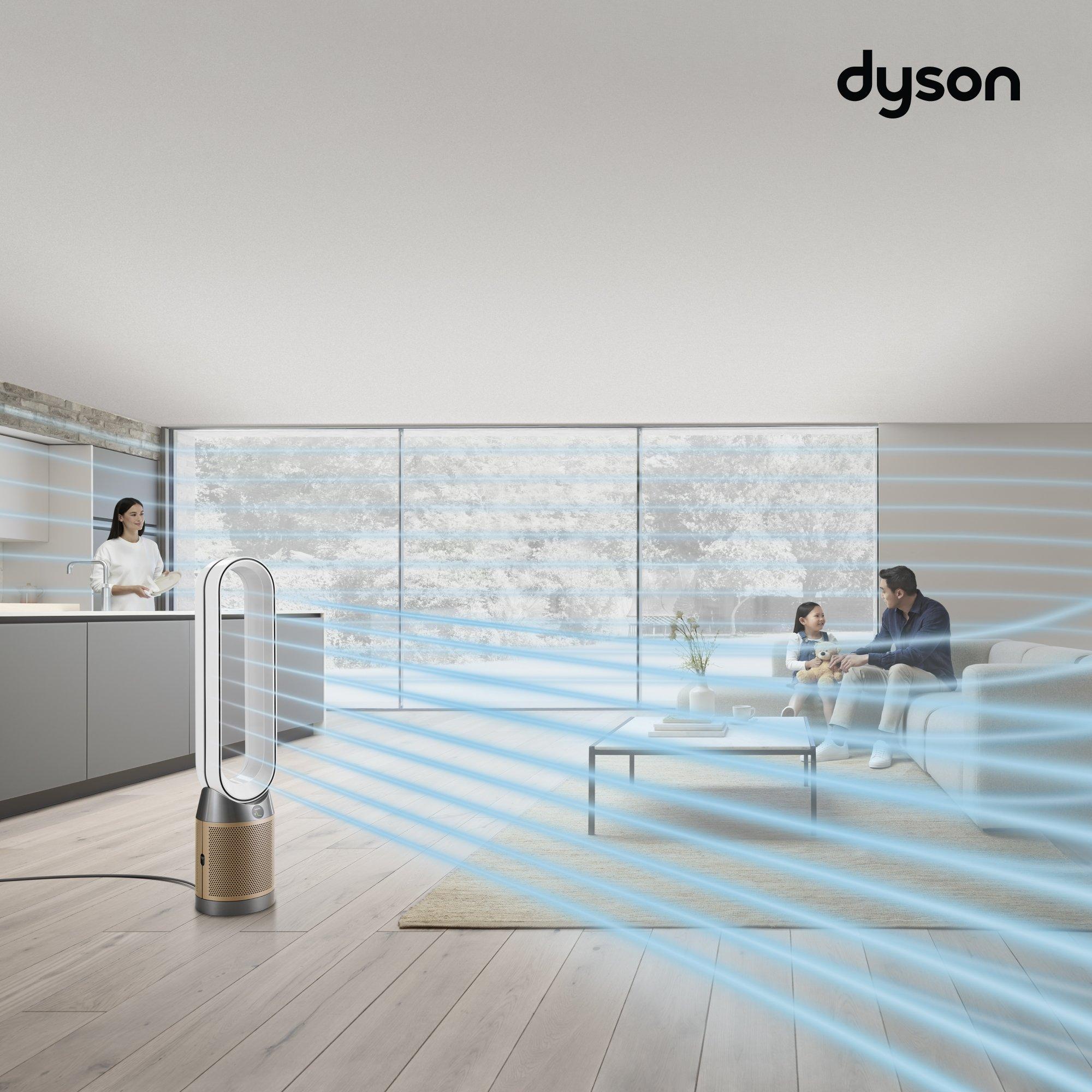 A Dyson air purifier is placed in a modern living room, emitting visible blue airflow lines, with a woman in the kitchen and a father and daughter sitting on a couch in the background.          Ask ChatGPT