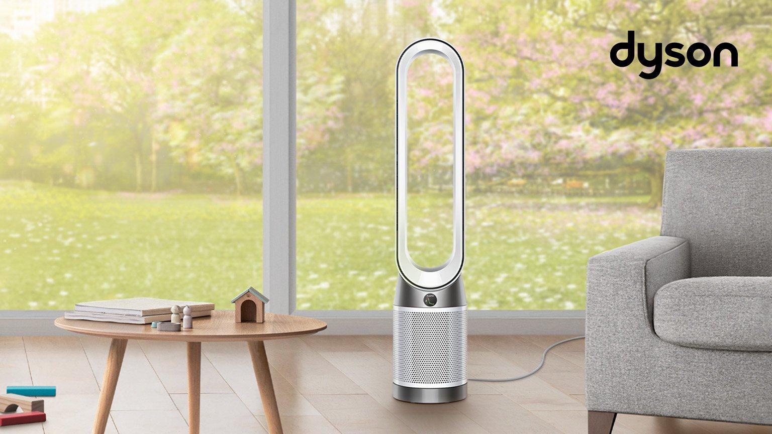 Dyson purifiers in the middle of the hall next to grey sofa and small wooden table with big window in the background
