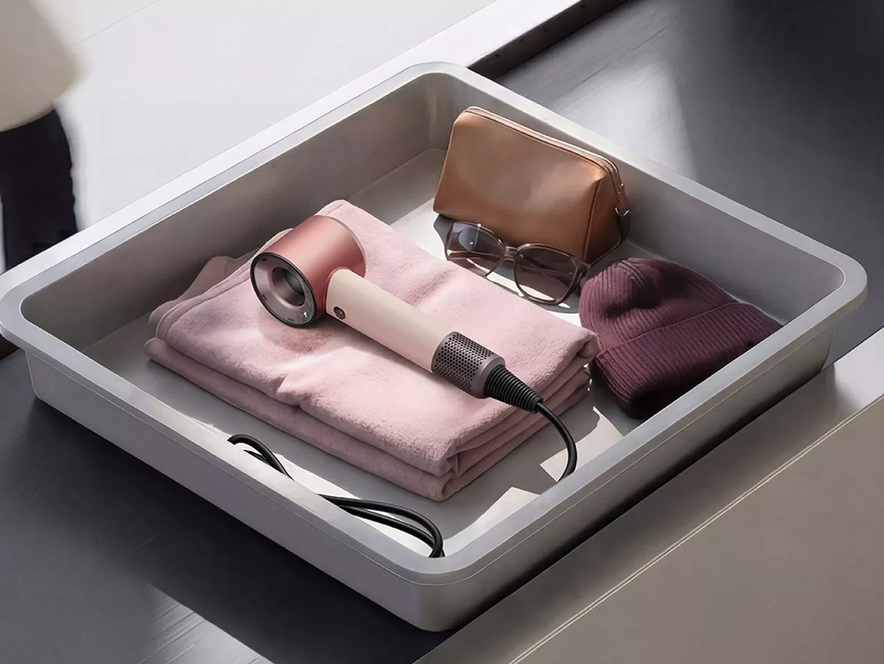 Airport security tray with hair dryer, folded jumper, glasses, beanie and storage pouch