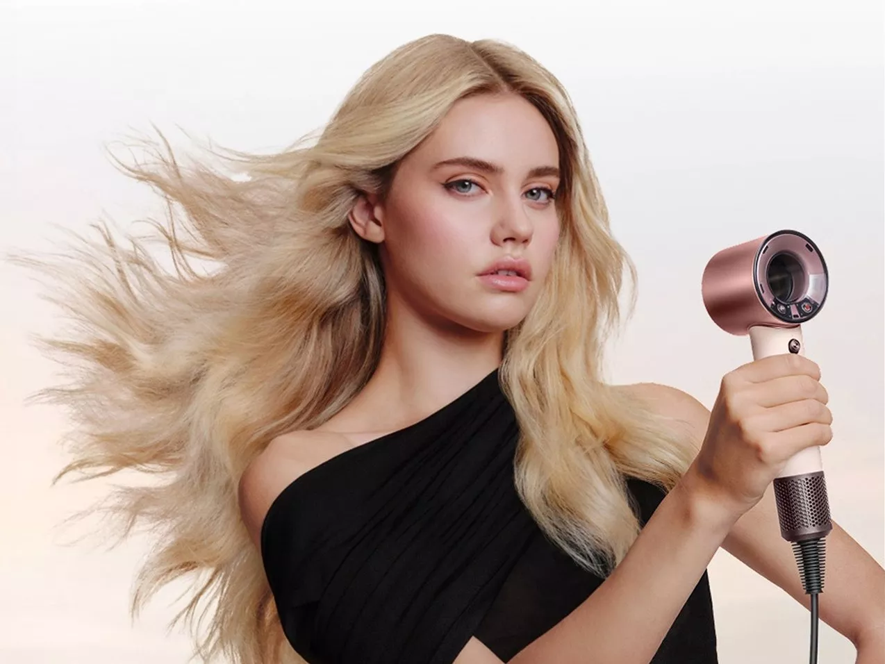 Blonde model with flowing hair holding a rose gold hair dryer, showcasing professional hair styling results