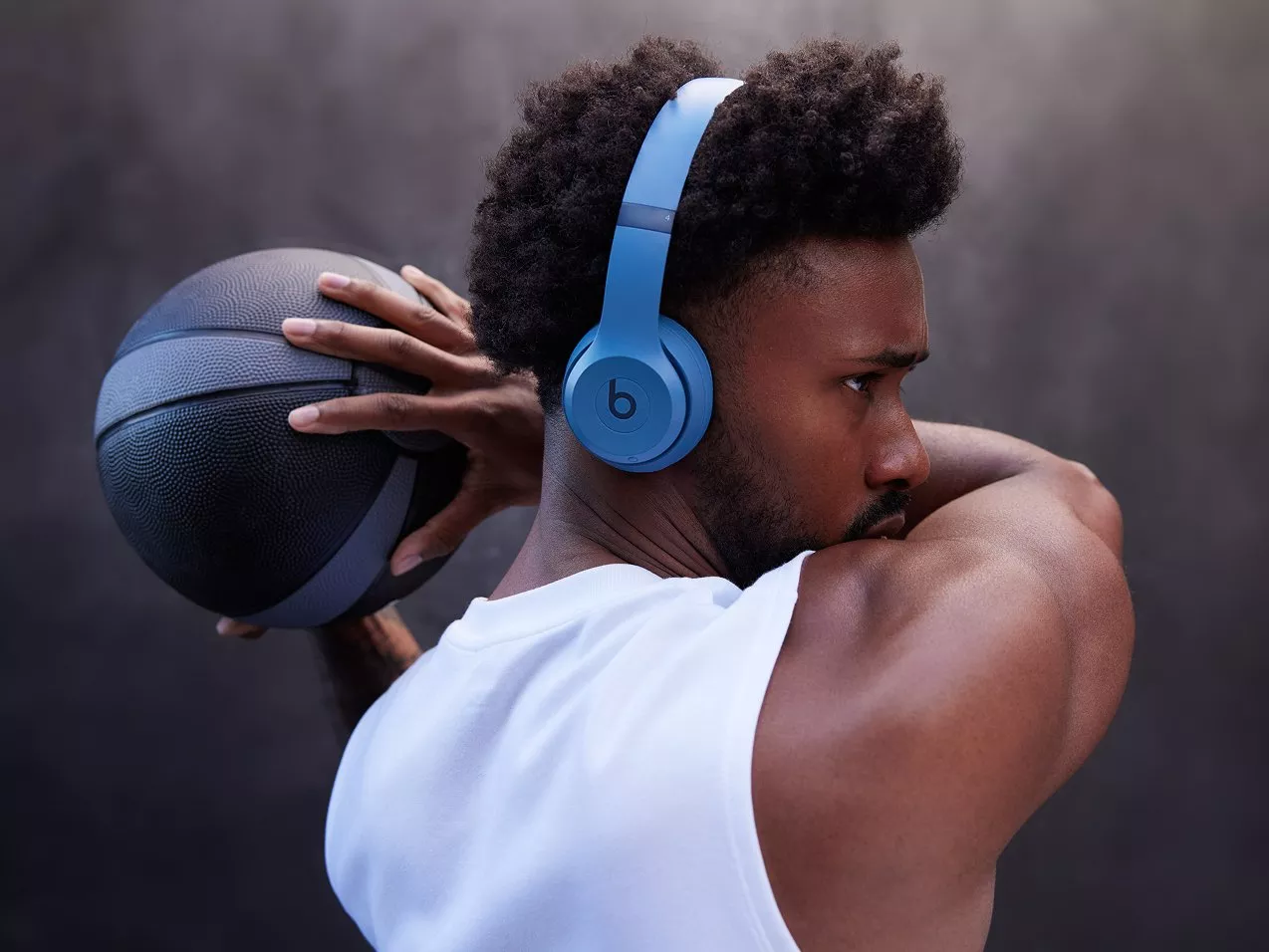 Athletic man wearing blue Beats headphones holds basketball behind head, focused fitness training portrait