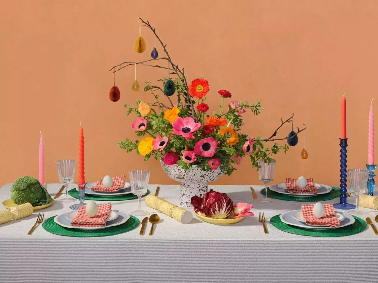 Elegant dining table setting with vibrant flowers, colourful candles, and decorative eggs on plates.