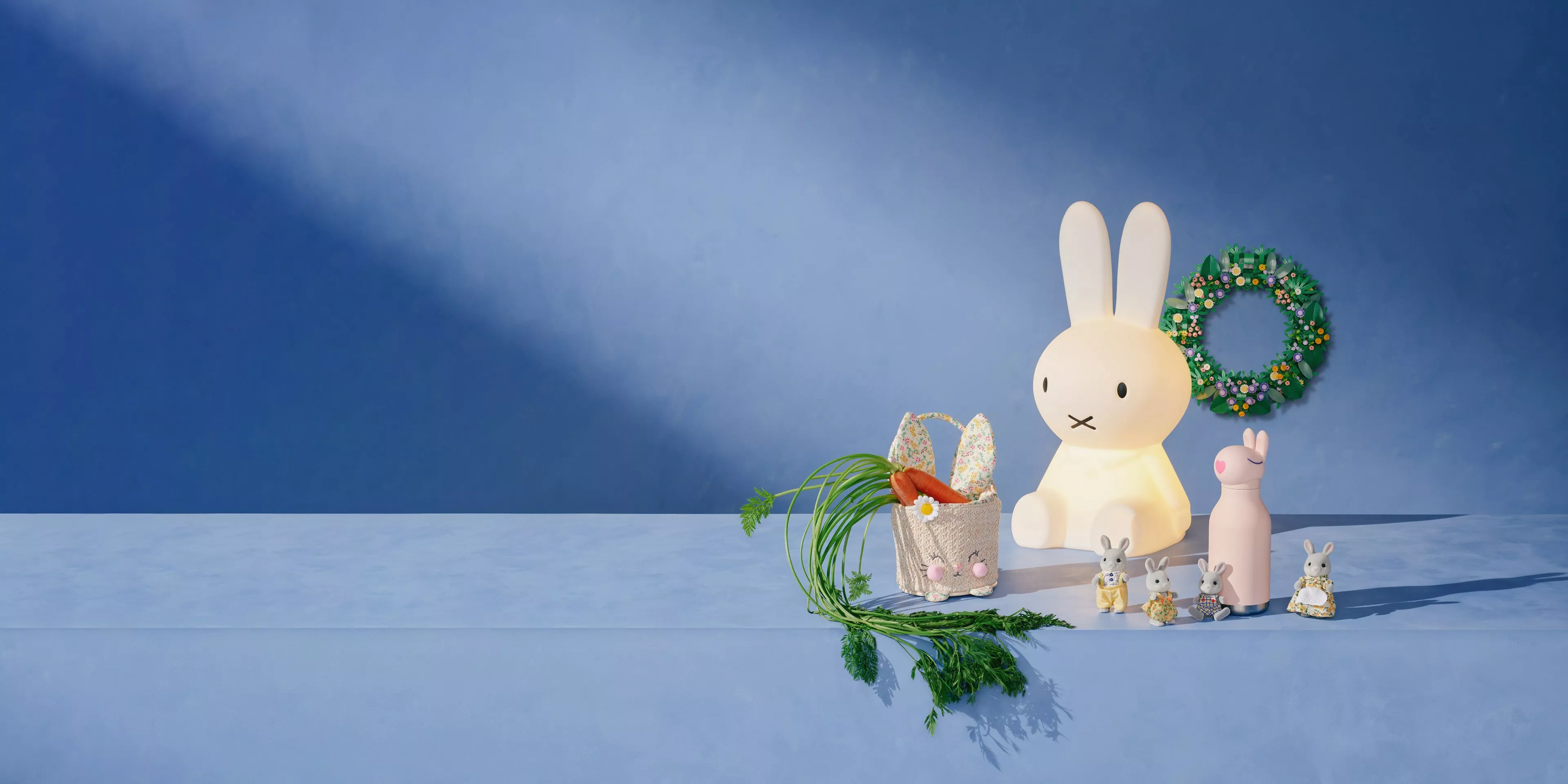 Cute rabbit-themed decor on a blue background, featuring toys, a wreath, and a basket filled with carrots.