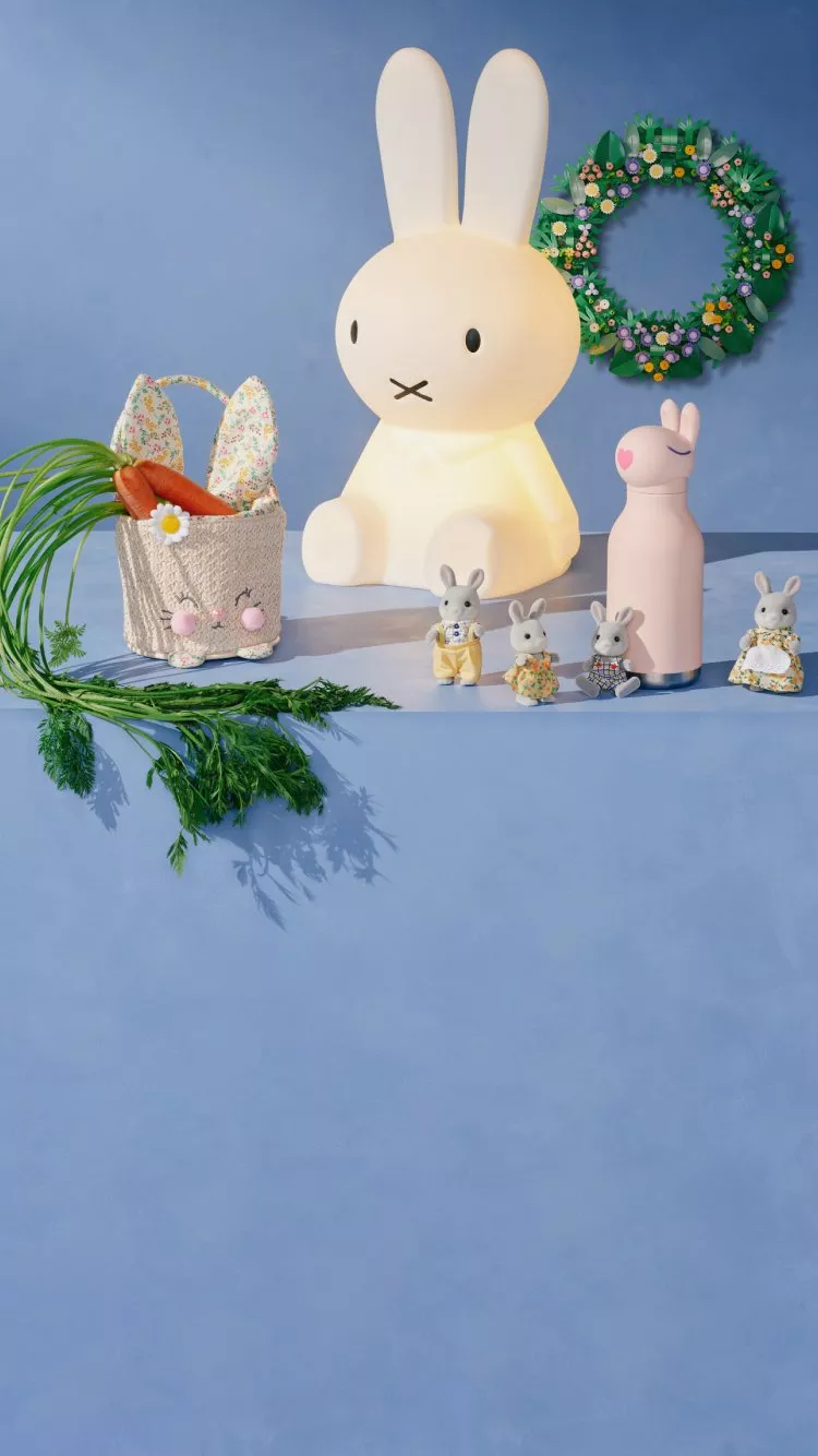 A cute rabbit lamp is surrounded by a wreath, a pink bottle, toy rabbits, and a basket with carrots on a blue background.