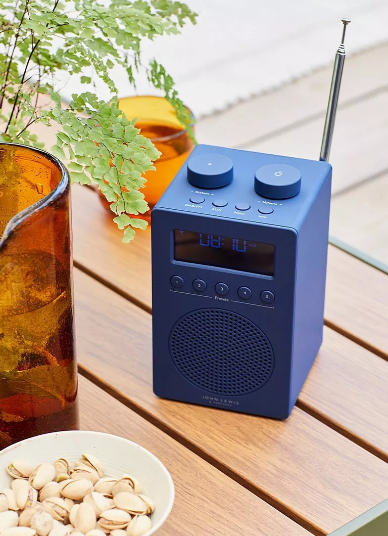 Blue portable DAB+ digital radio with telescopic aerial on wooden outdoor table, beside plant and snacks