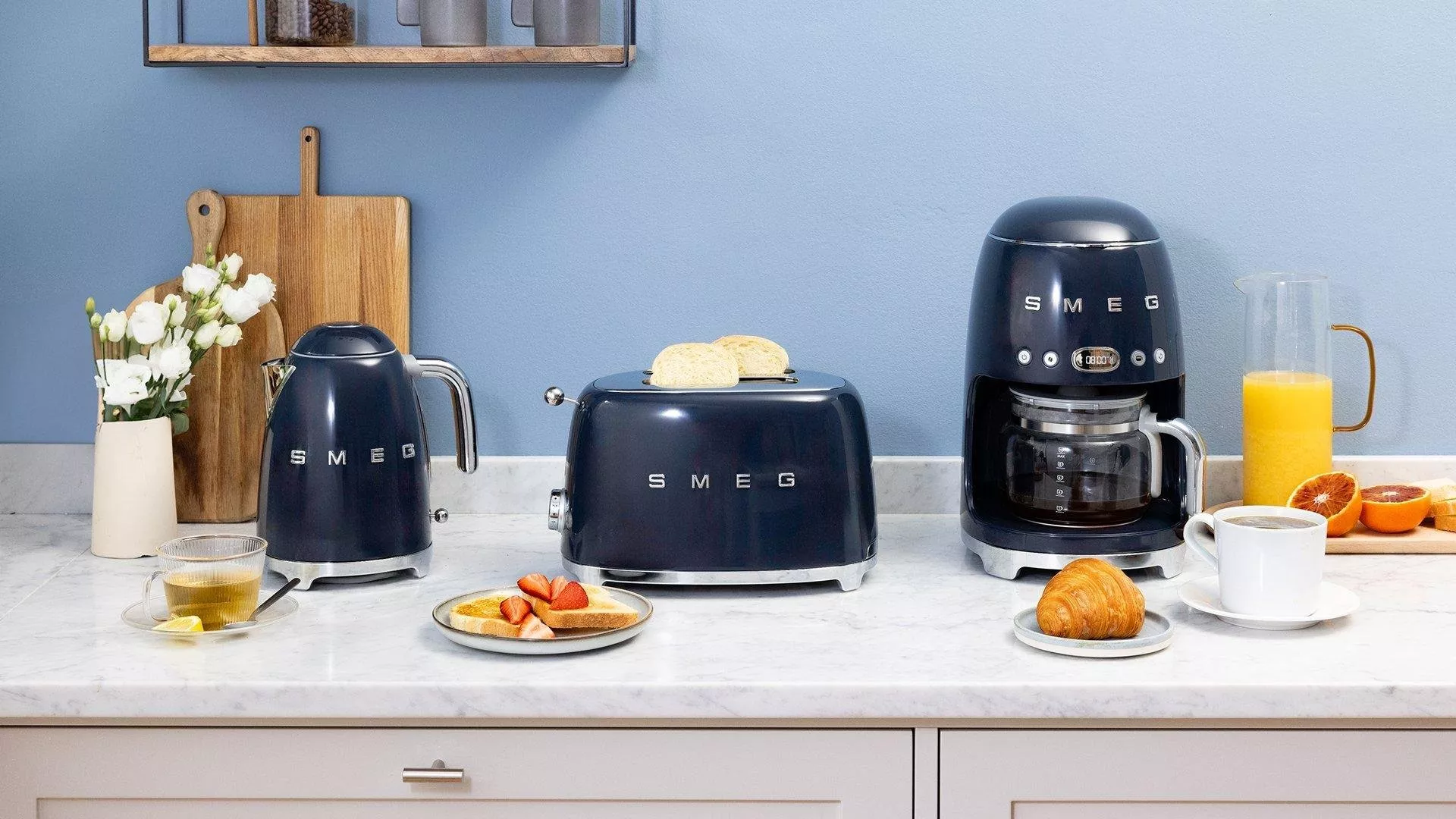 Stylish kitchen scene with navy SMEG appliances, coffee, toast, croissant, and juice on a marble countertop.
