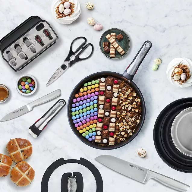 Marble surface with kitchen items including a knife, pans, and meringue nests topped with chocolate eggs.