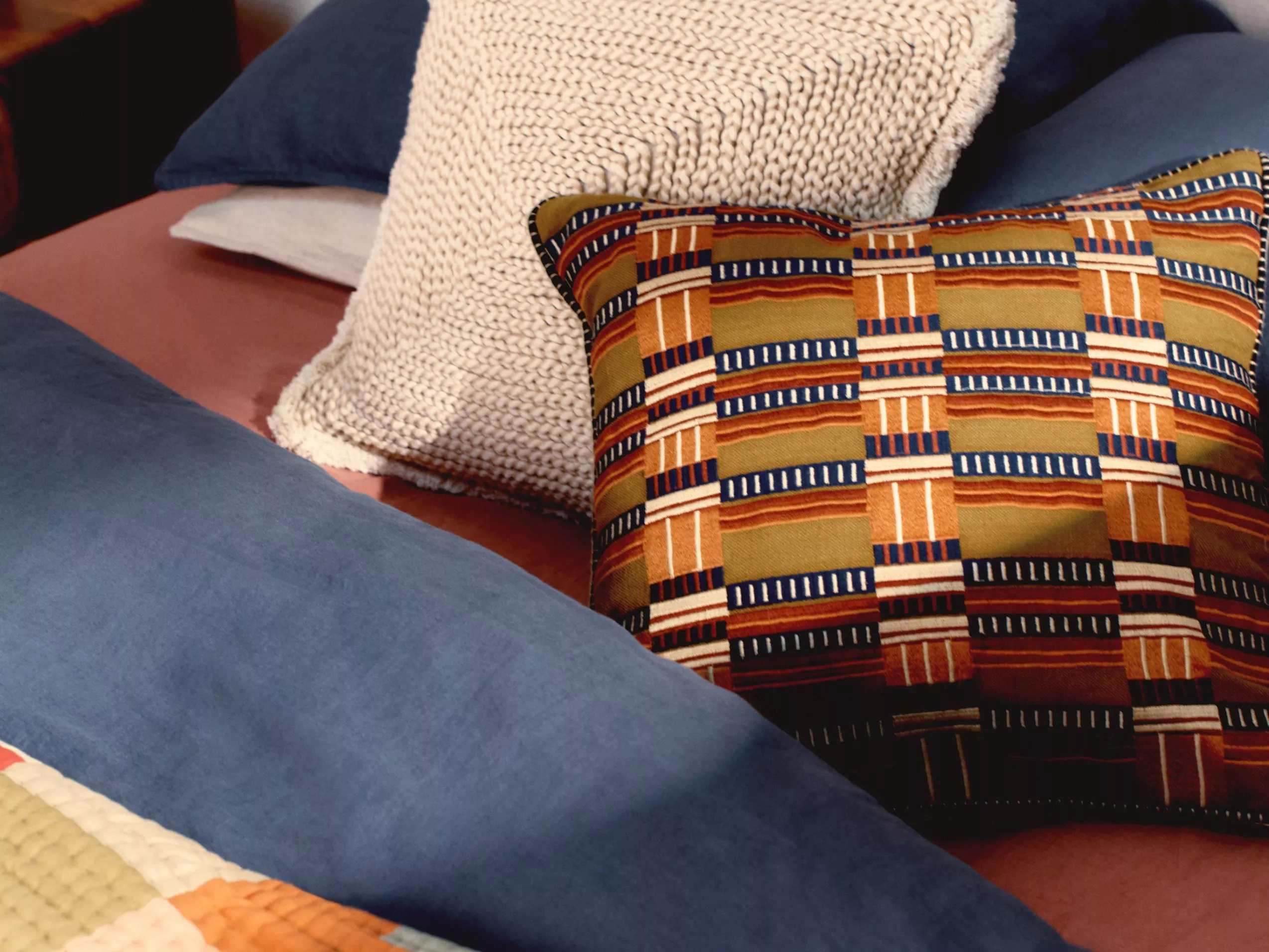 Textured cushions with colourful patterns on a bed with blue and pink bedding, creating a cosy look.