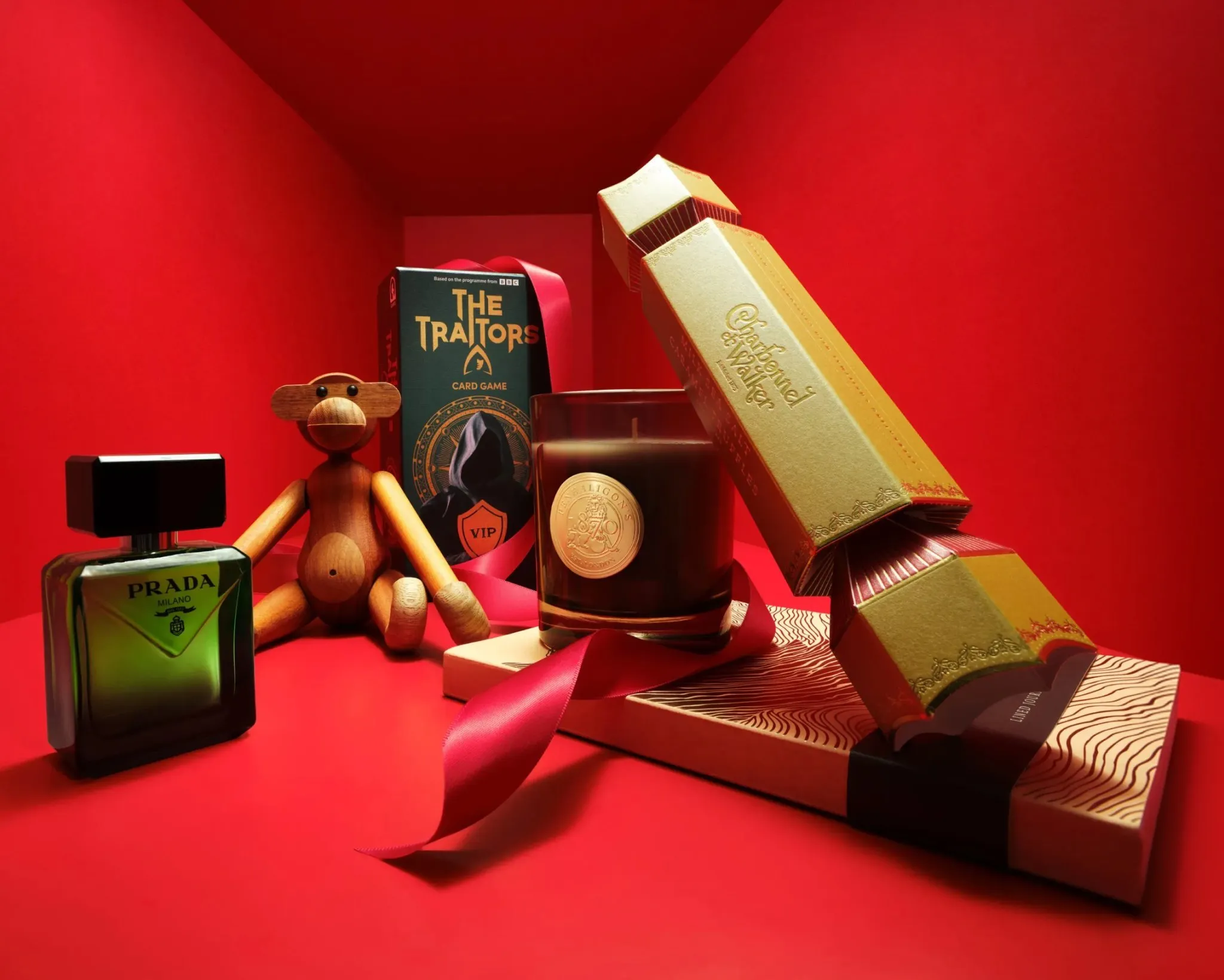 Luxury Christmas gift set on red background with Prada perfume, candle, wooden toy and card game box