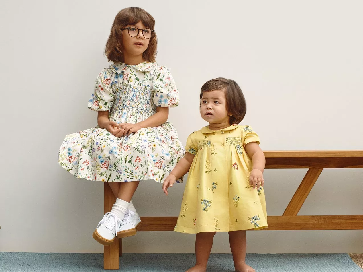 Two children in colourful outfits. One wears a red jacket and striped trousers, the other a floral skirt and top.