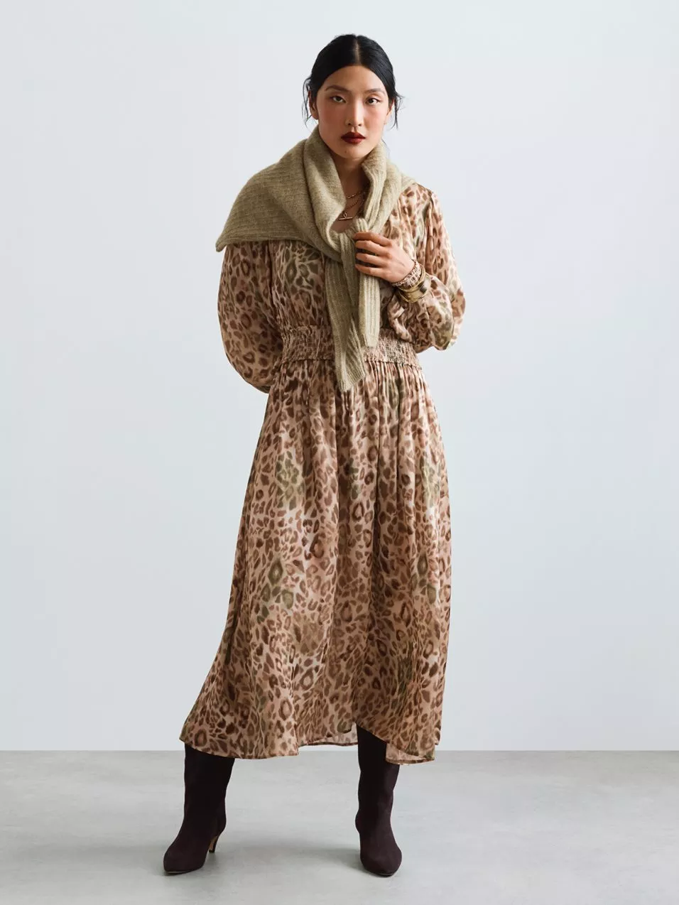 Fashion model in leopard print midi dress with beige scarf and ankle boots, studio portrait on grey background