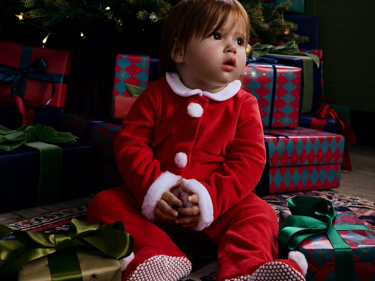 Toddler sitting in front of Christmas tree, dressed in red Christmas outfit