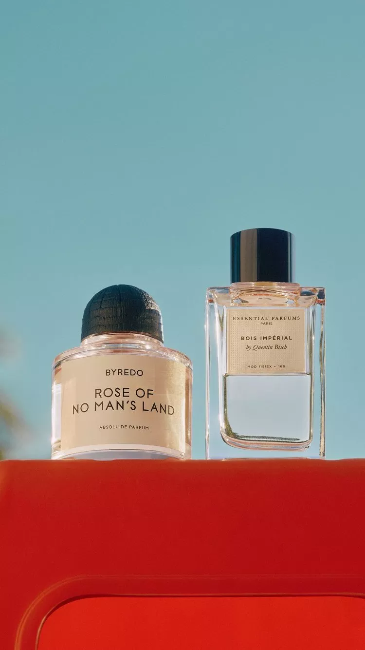 bottle of byredo - rose of no man's land perfume on a red table with sunny palm trees behind