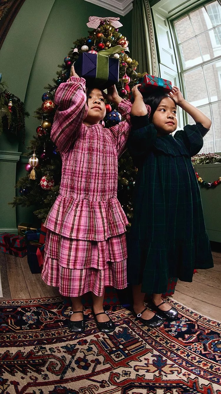 Two girls in Christmas dresses holding gifts above their heads