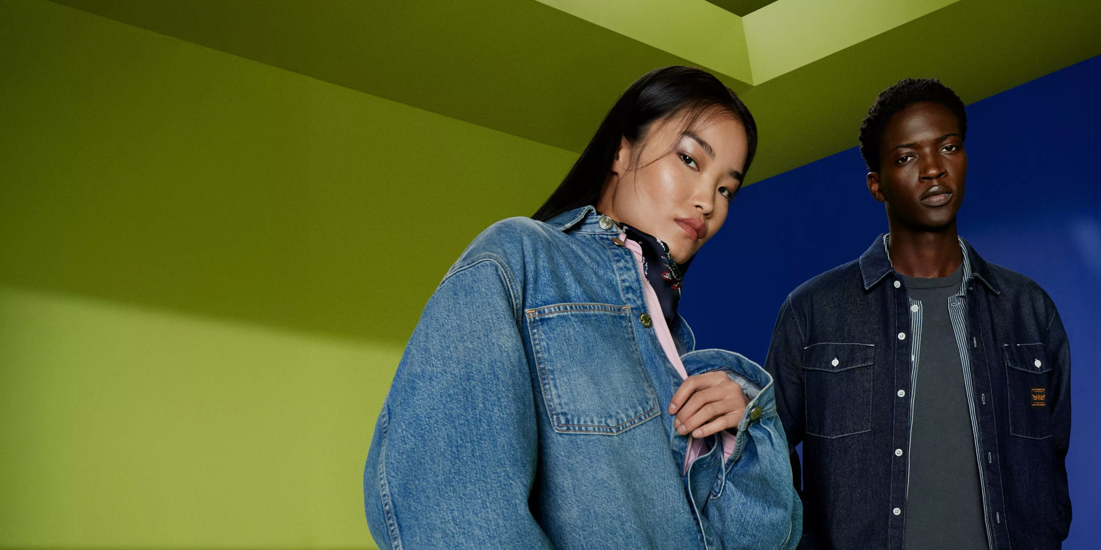 Fashion models in denim jackets and jeans posing against bold blue and green studio backdrop, casual streetwear style