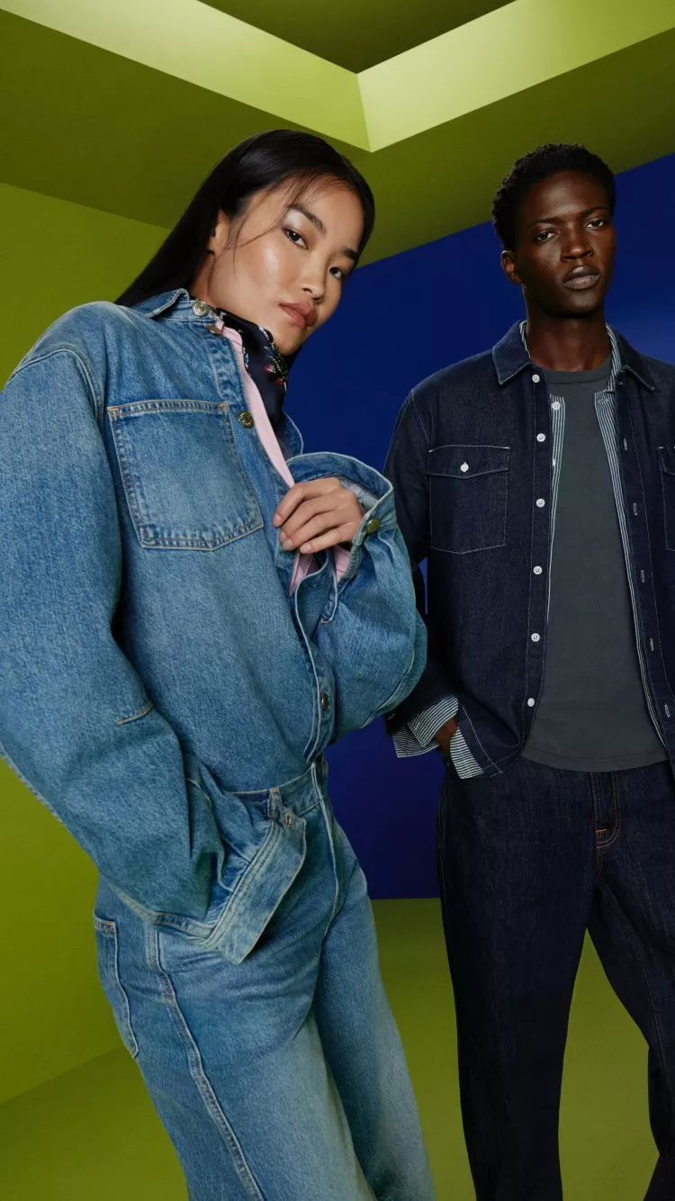 Two fashion models in denim jackets and jeans posing in a studio with bold green and blue geometric backdrop