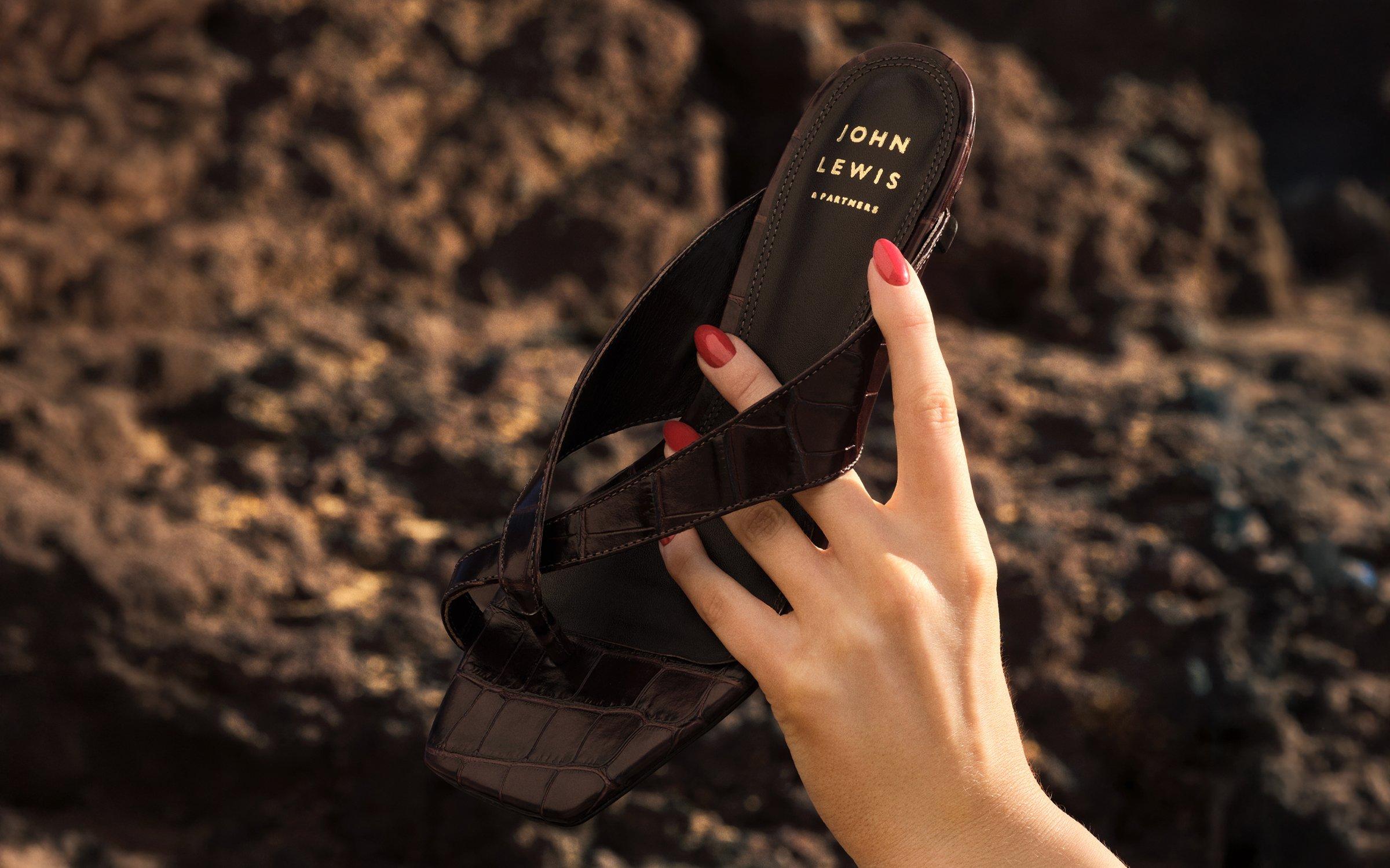 womens decrotive cream suede sandal sitting on volcanic rock on a sunny day