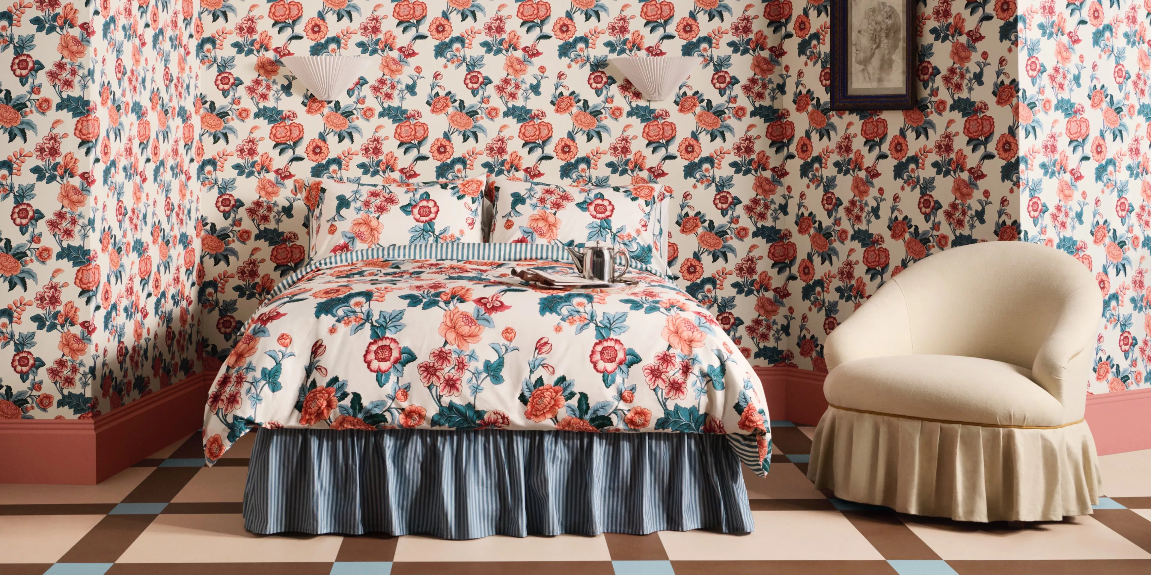 Floral-themed bedroom with matching wallpaper and bedding, featuring a cosy cream chair and a chequered floor.