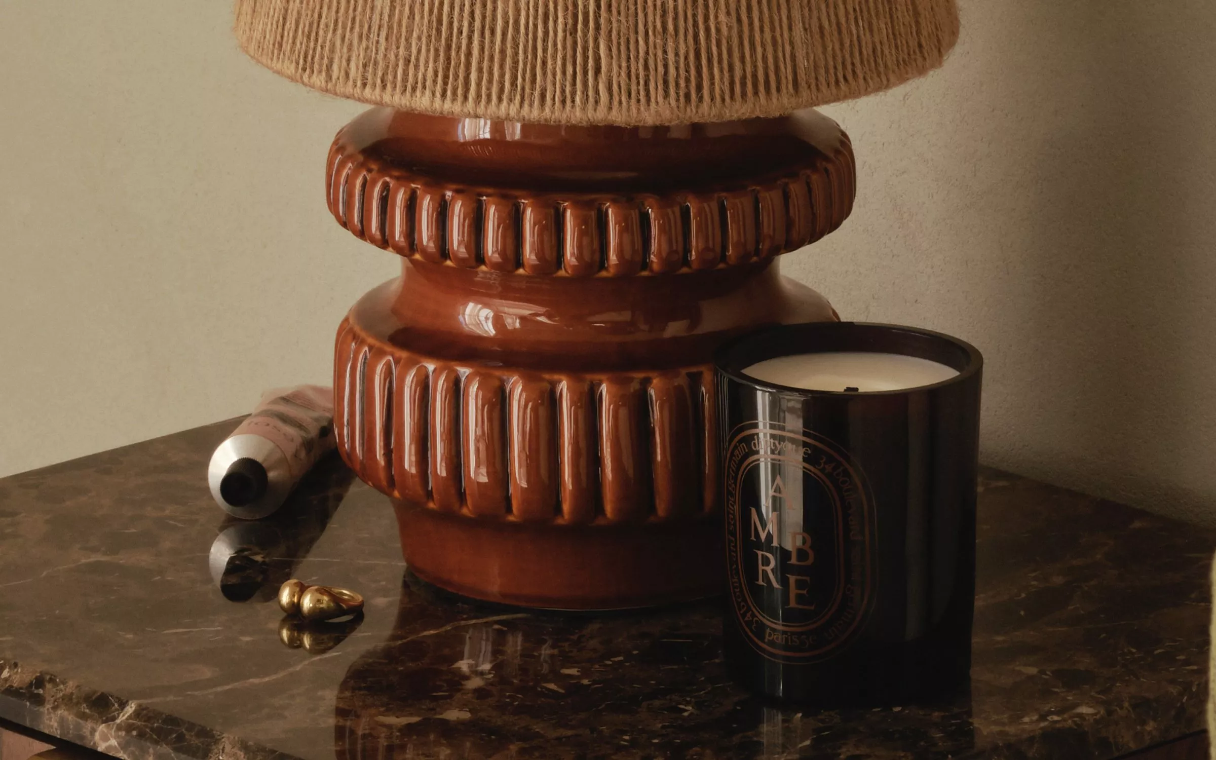 Black scented candle beside vintage brown ceramic lamp on marble side table, cosy minimalist home décor close-up