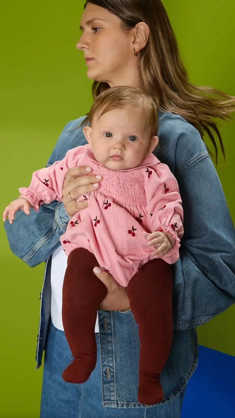 Smiling baby boy in blue and yellow striped knitted romper, sitting on carpet against neutral studio backdrop