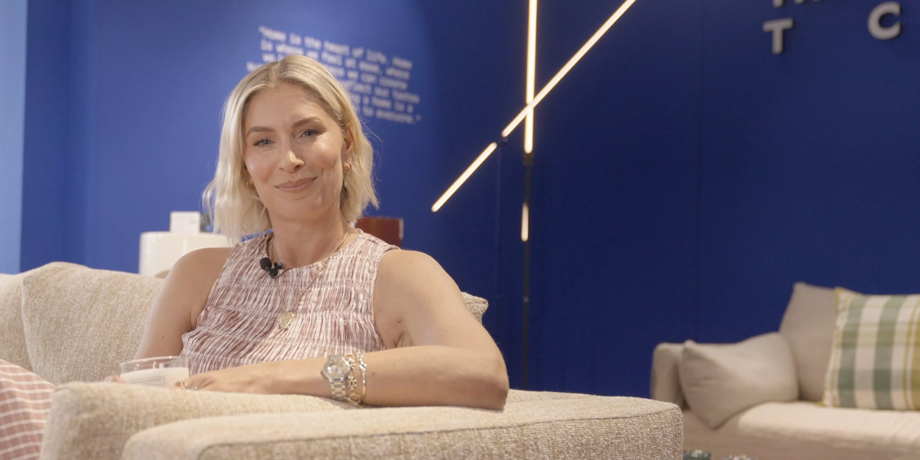 Louise Boyce seated on a sofa in a modern showroom, showcasing stylish interior design and lighting display.