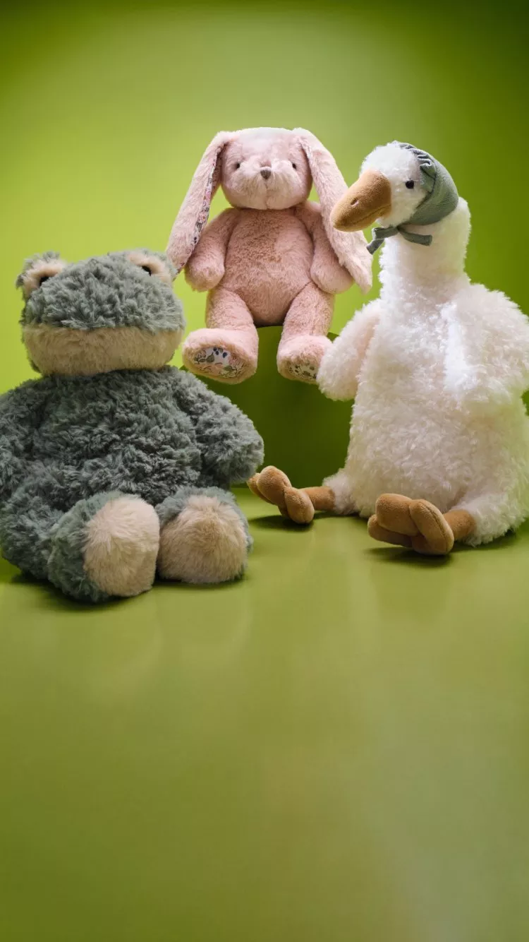 Soft plush teddy bear, pink bunny and white duck toy sitting on green background, cute nursery decor photo