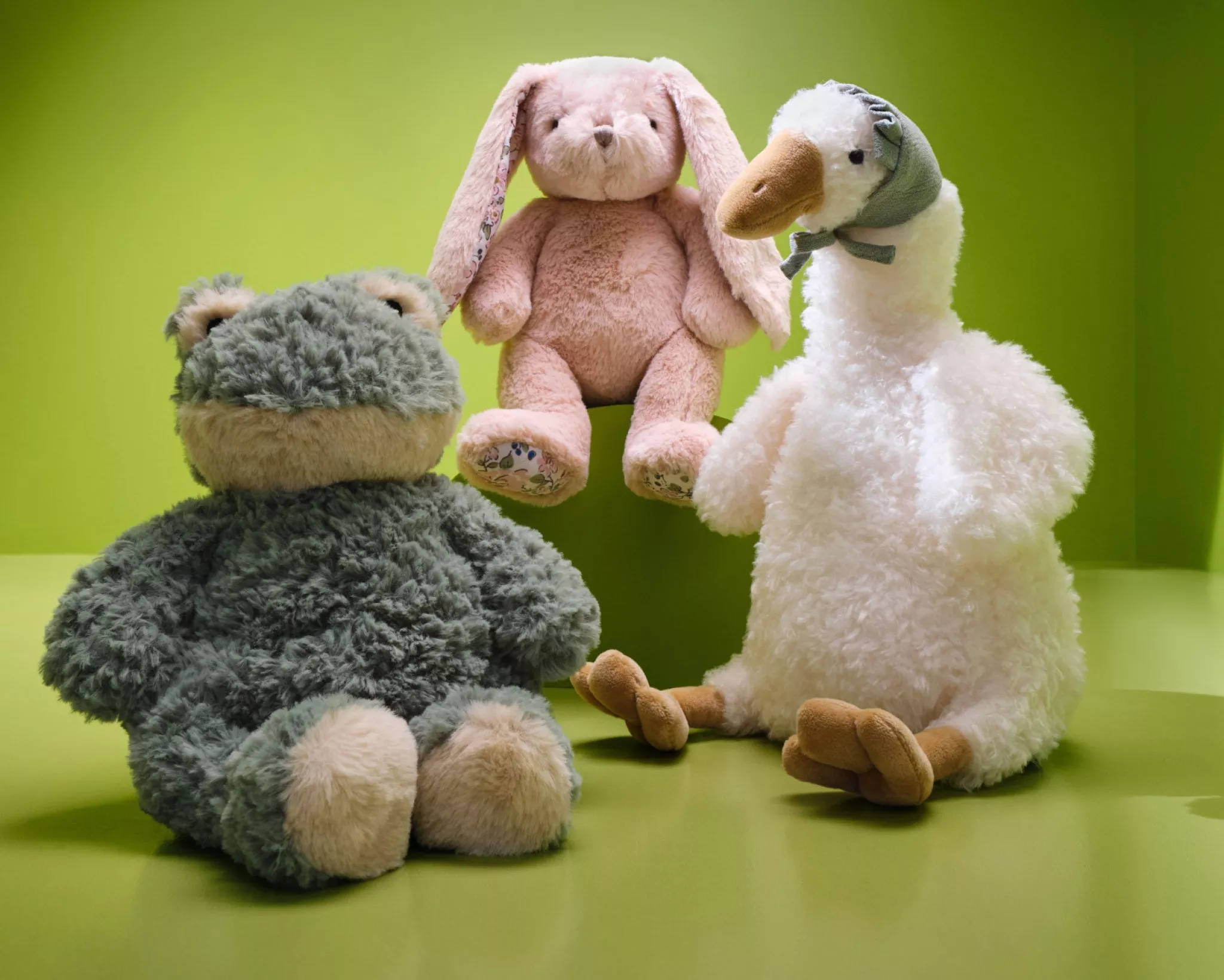  Three Mon Ami plushie toys, a frog, pink rabbit, and white goose, on a green background