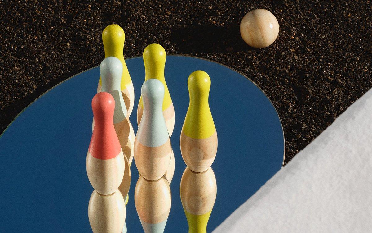Wooden skittles on a mirror top next to a wooden skittle ball.