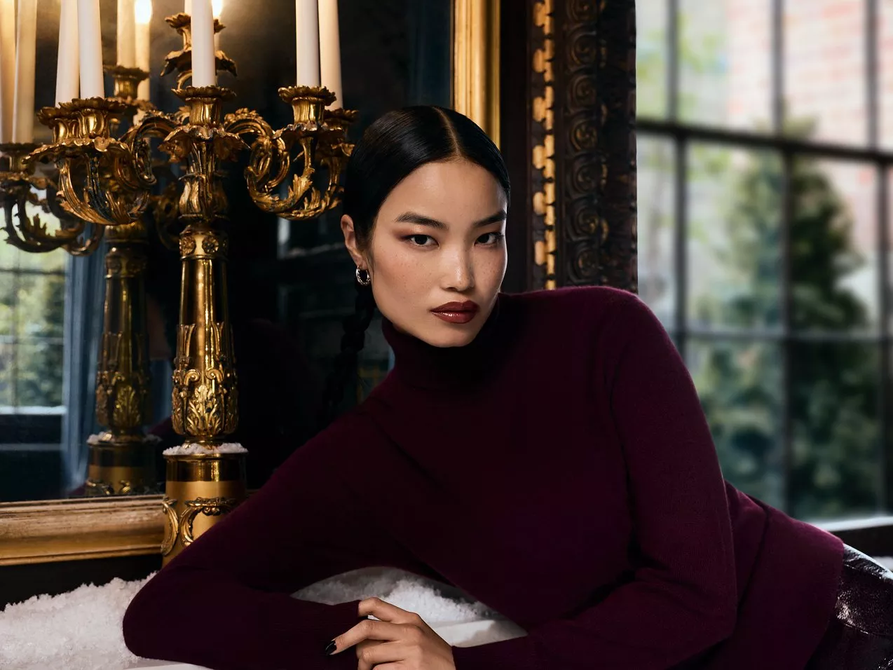 Woman in burgundy jumper leaning against a fireplace ledge