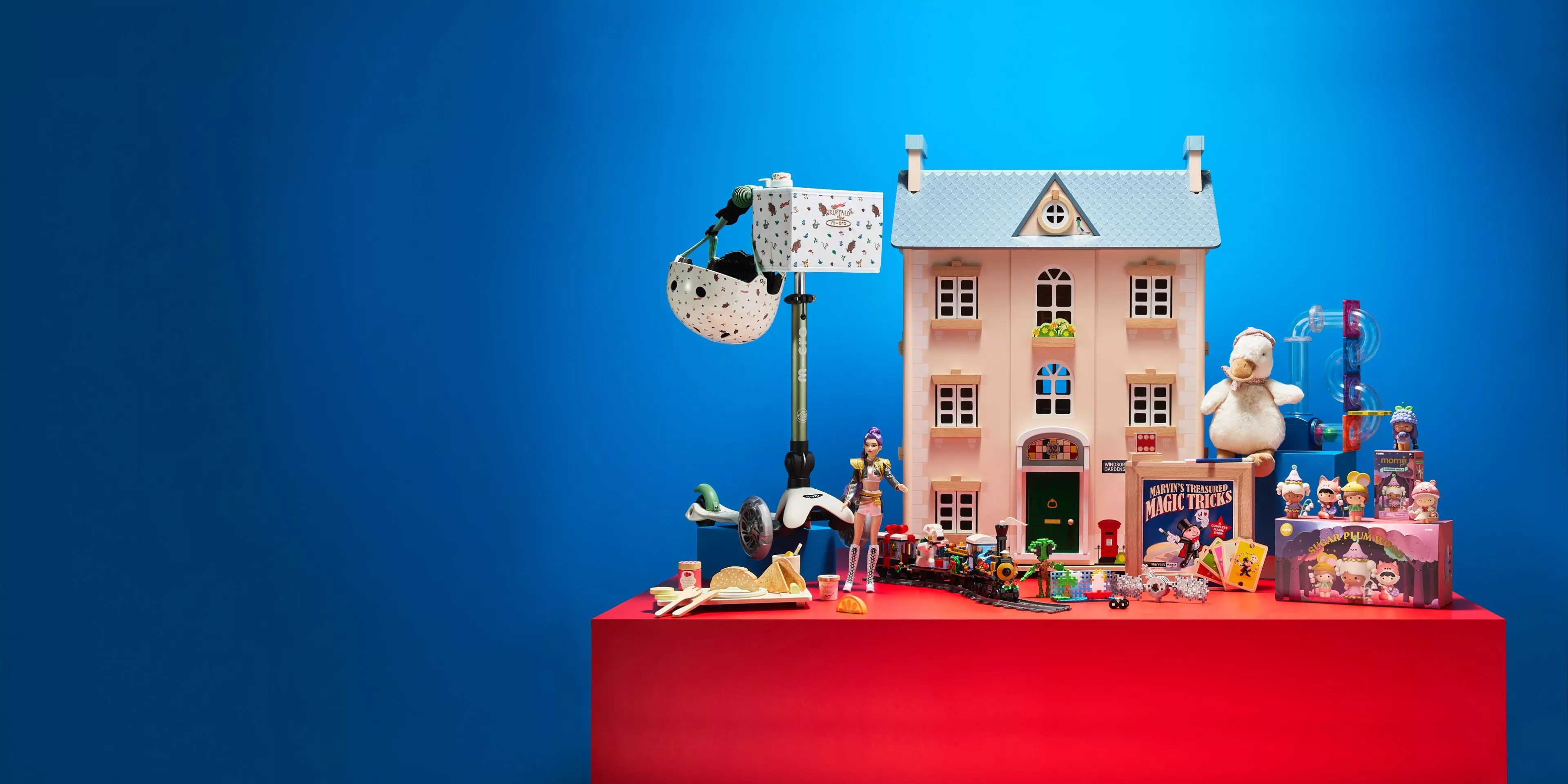 Toy dollhouse and assorted children’s toys on red table against blue background, colourful playroom display