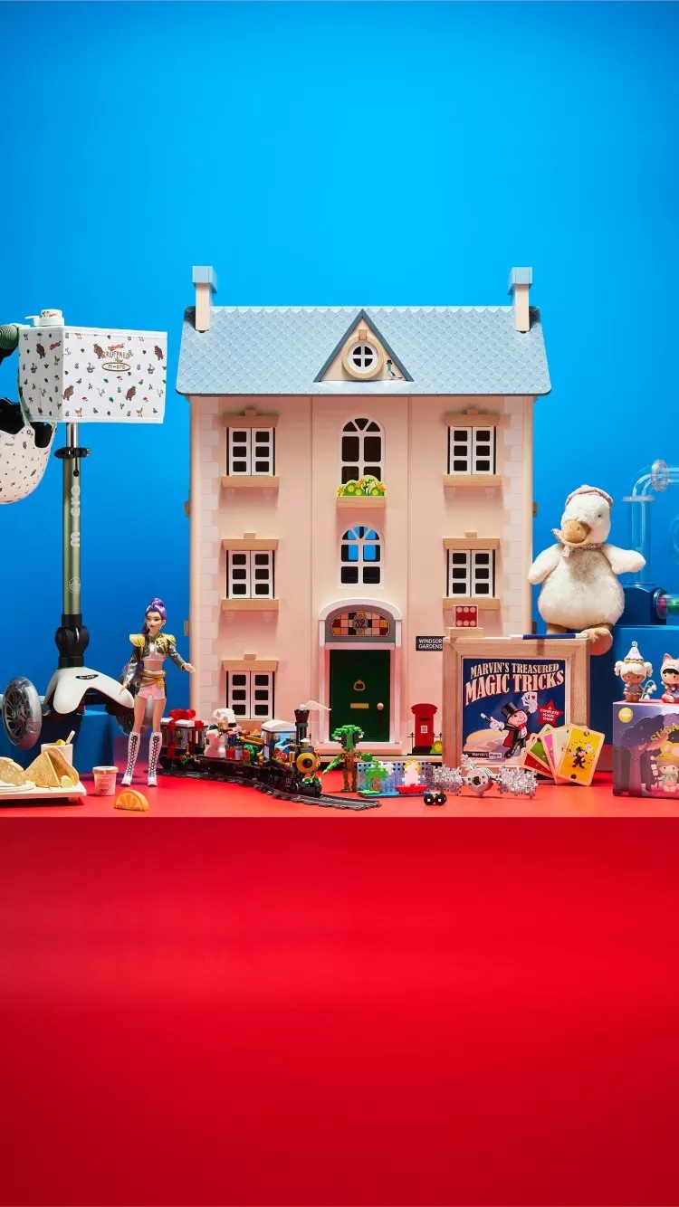 Toy dollhouse and assorted children’s toys on red table against blue background, colourful playroom display