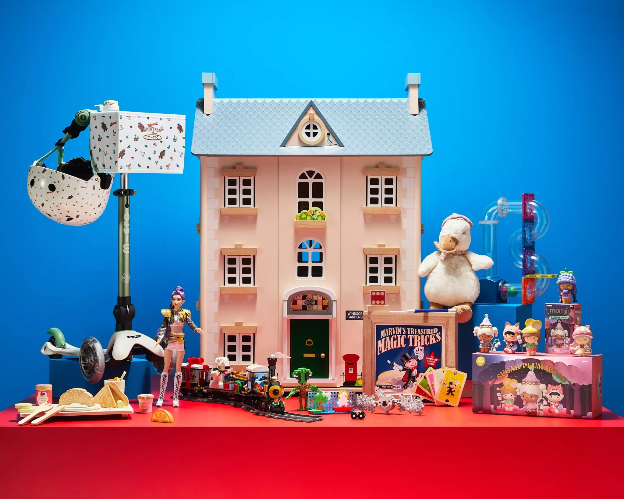 Toy dollhouse and assorted children’s toys on red table against blue background, colourful playroom display