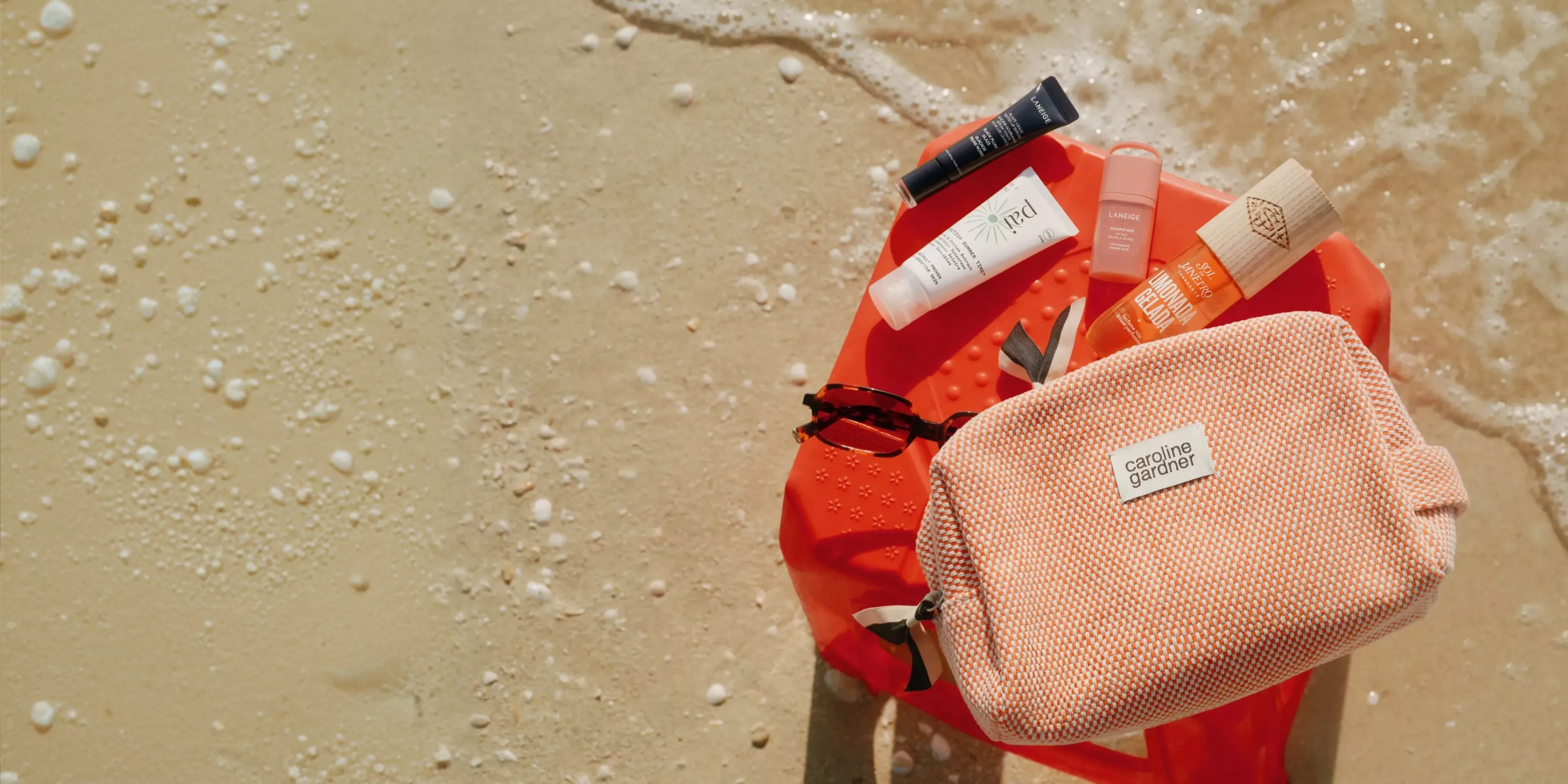 travel bag with beauty products layed out on the sand