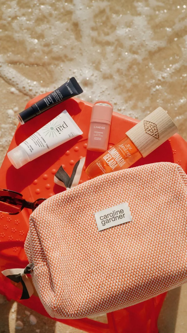 travel bag with beauty products layed out on the sand