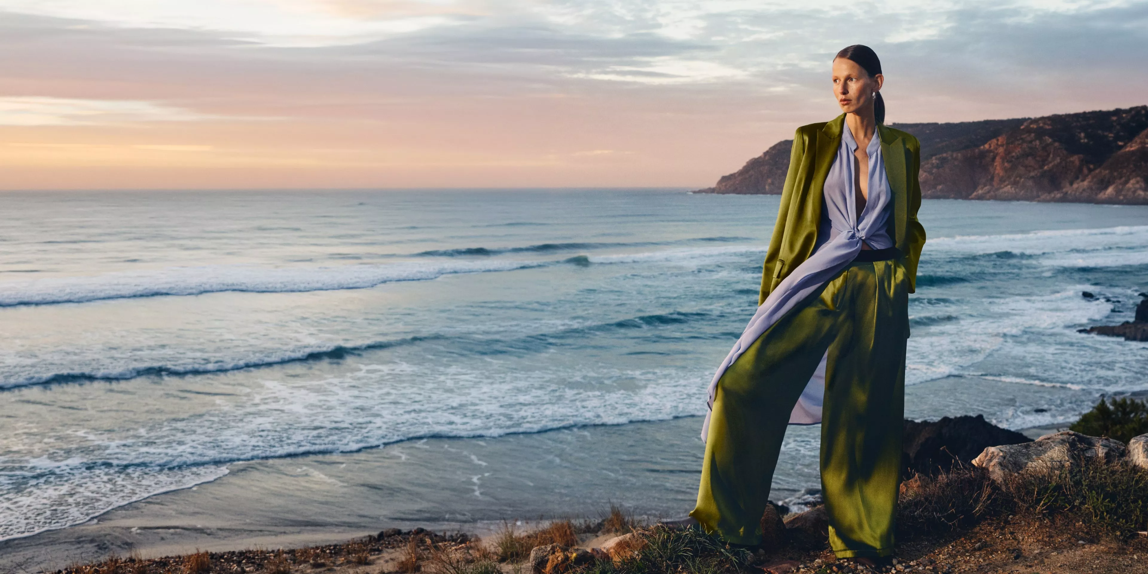 women wearing a green trousersuit with a beach behind her