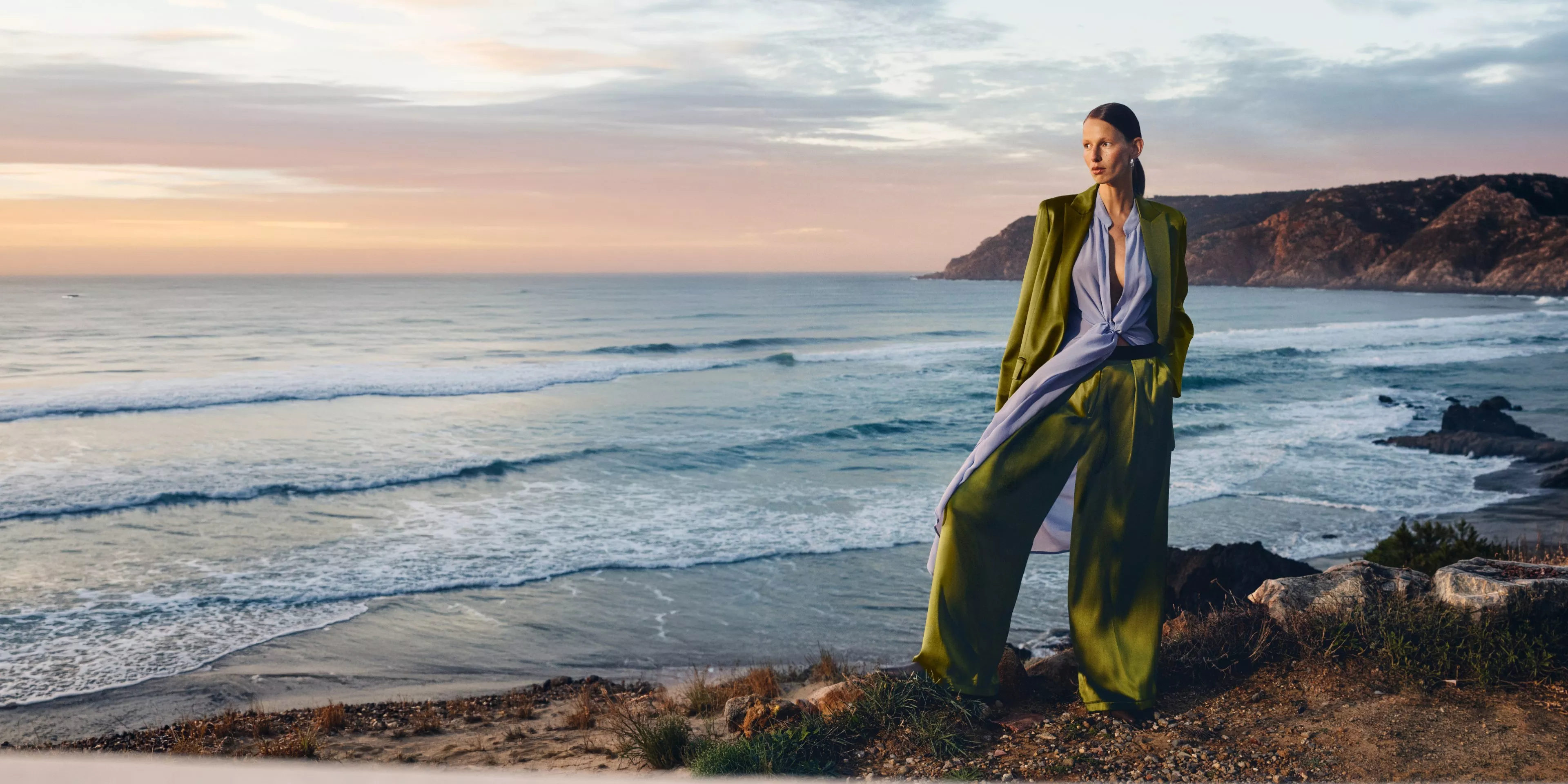 women wearing a green trousersuit with a beach behind her