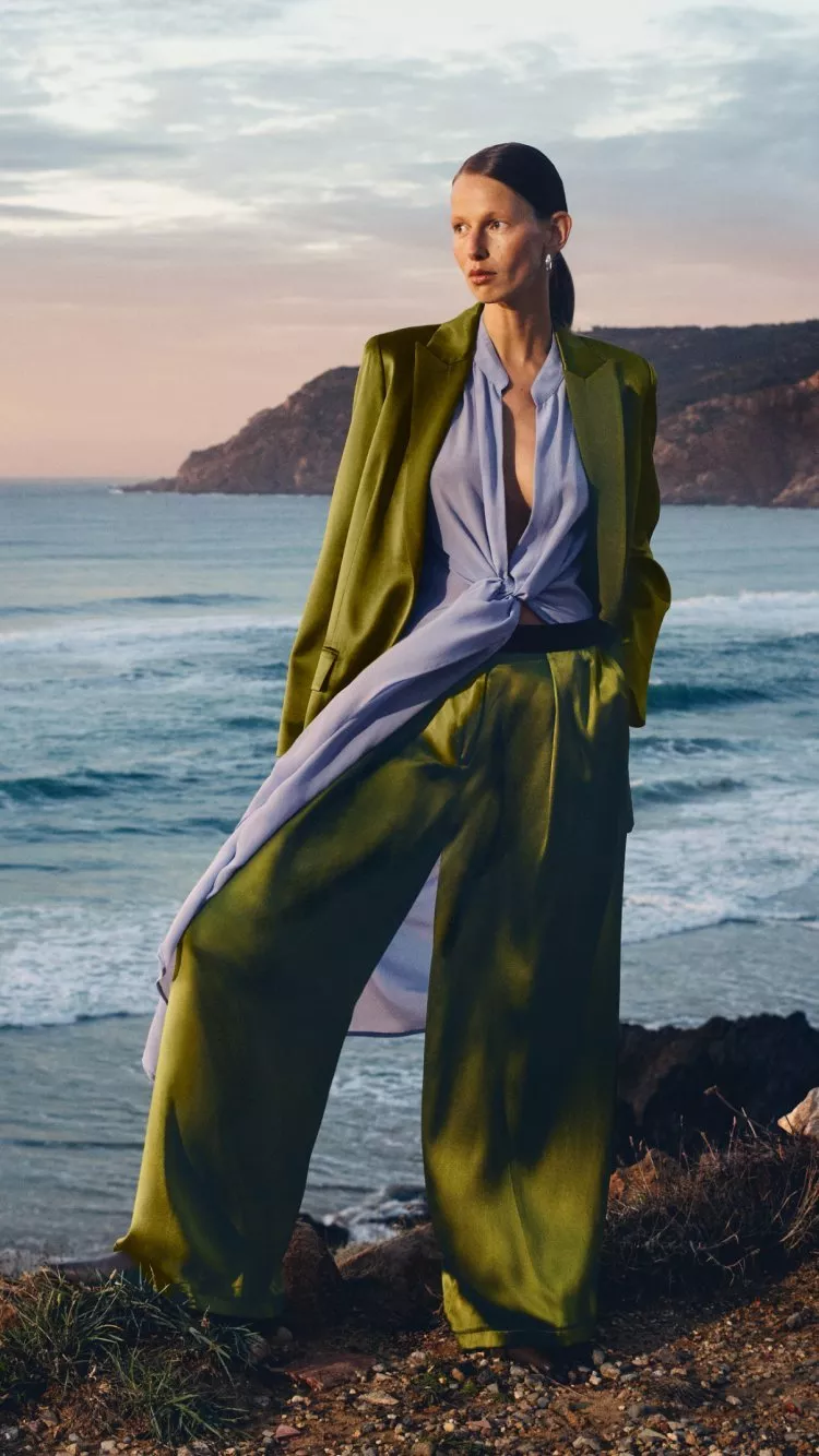 women wearing a green trousersuit with a beach behind her