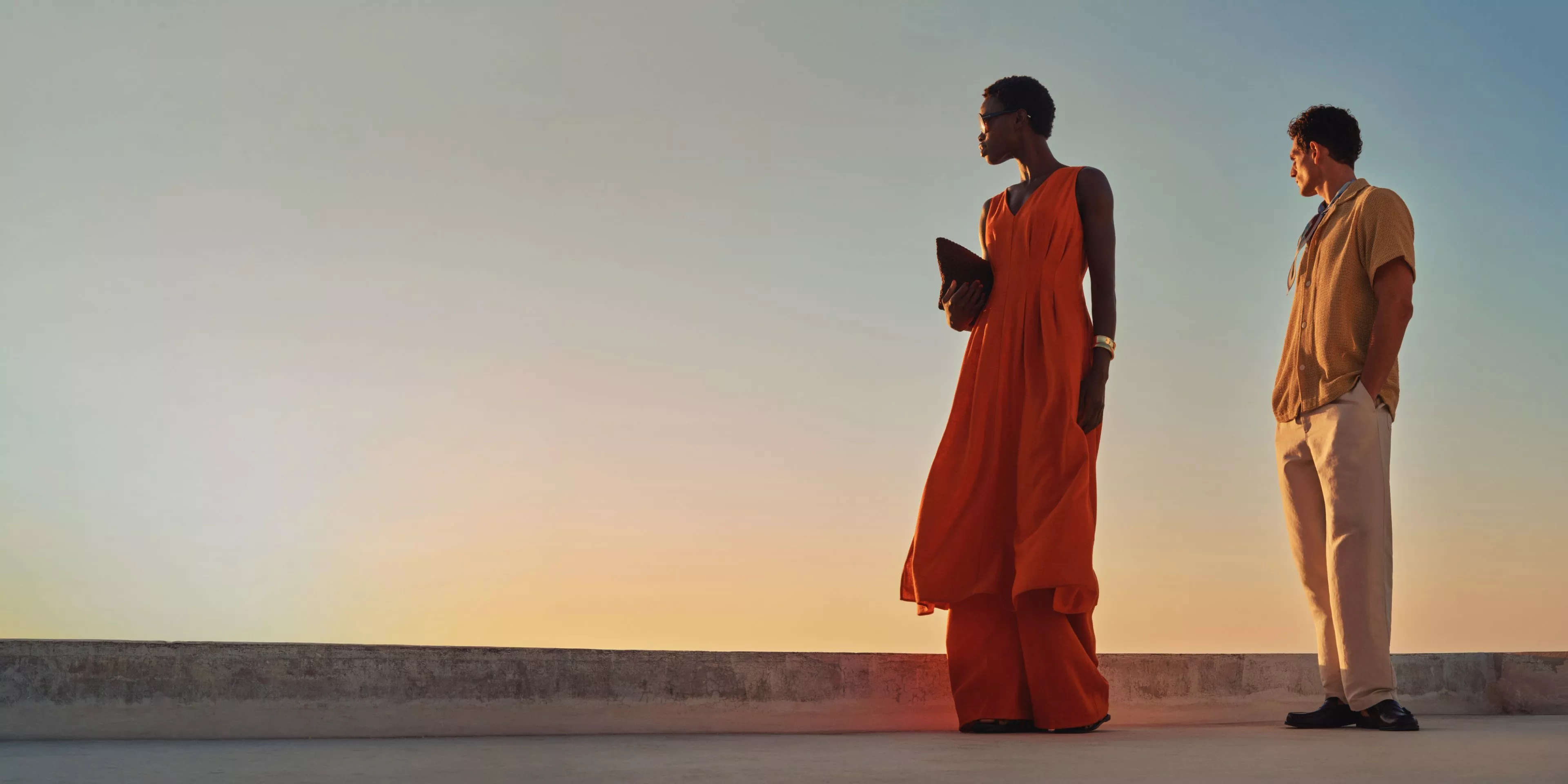 women wearing a bright orange dress and trousers and a man wearing smart short sleeve shirt and trousers
