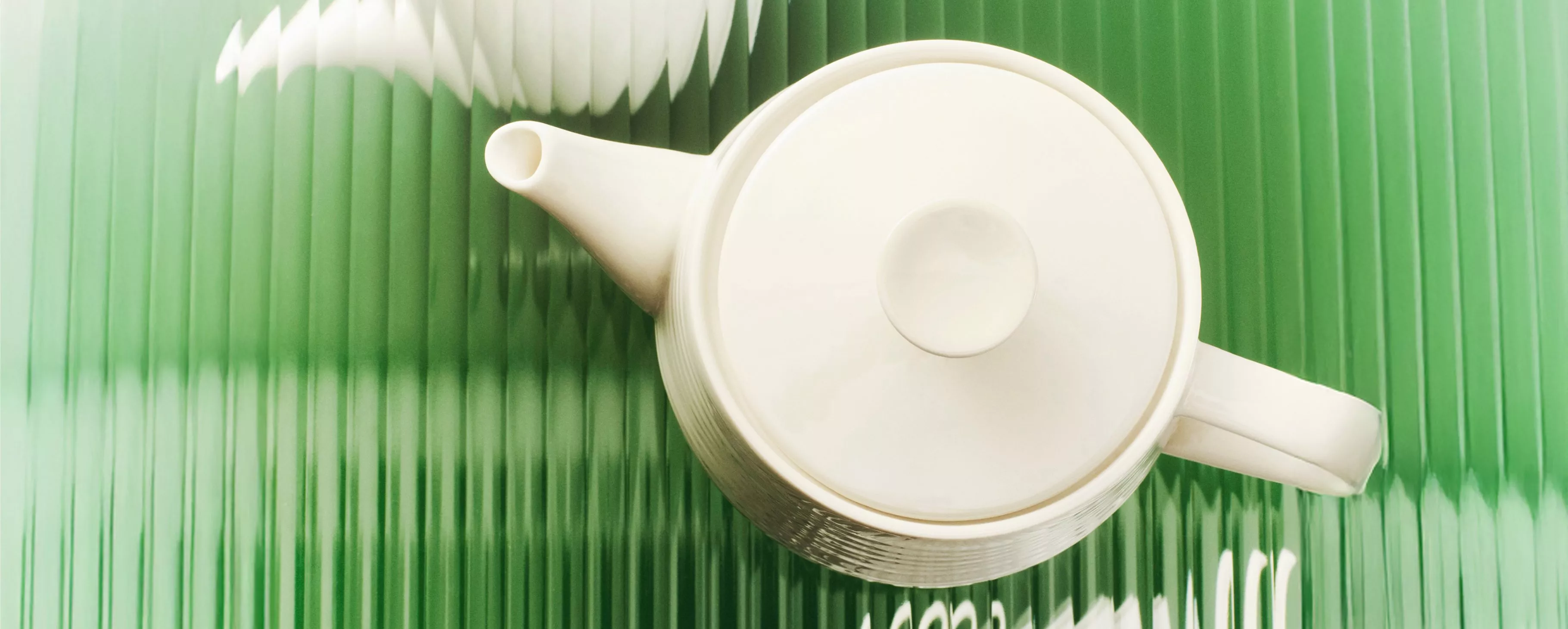 A white ceramic teapot viewed from above on a green, vertically textured background.