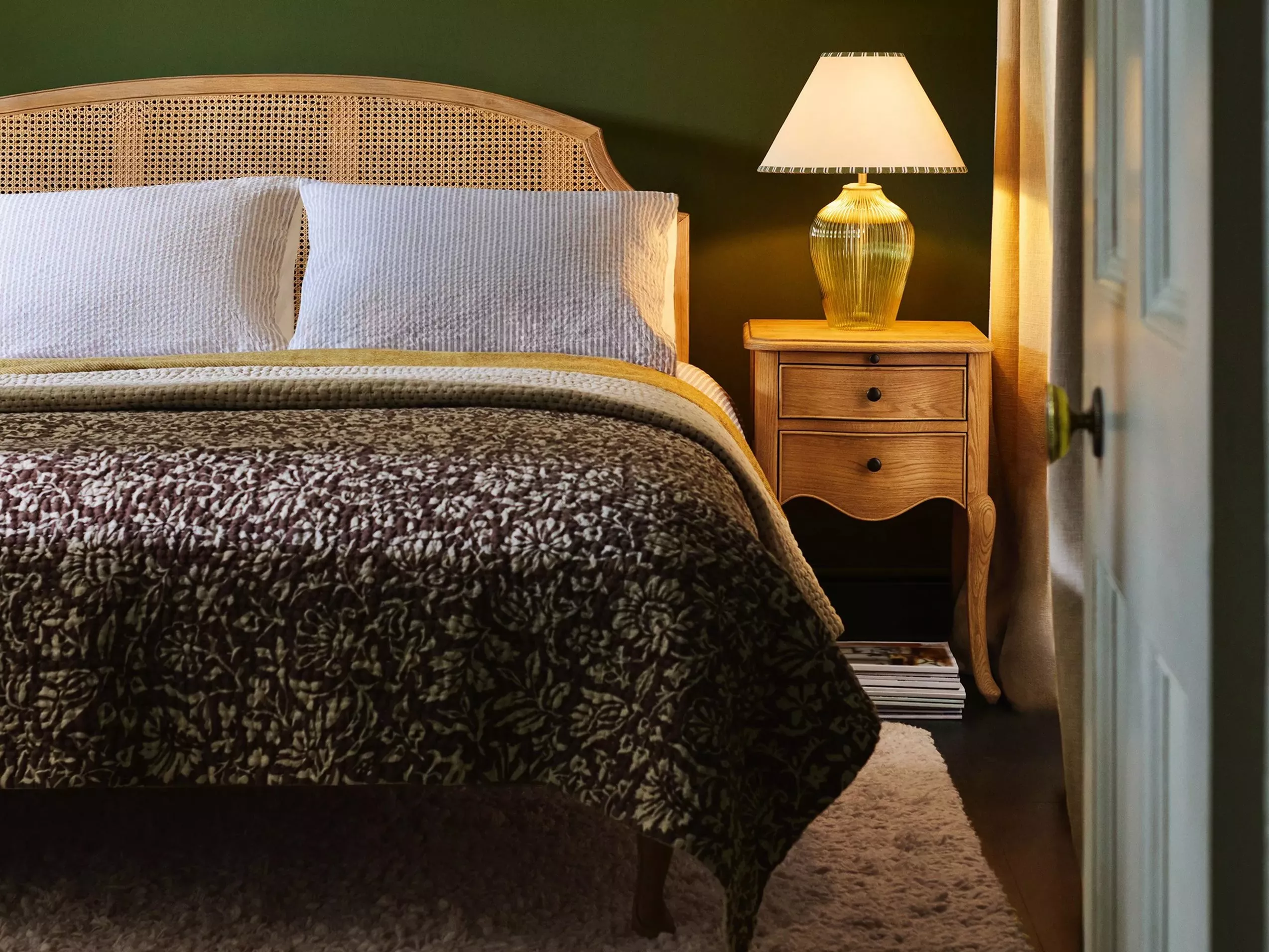 Cosy bedroom with a patterned quilt, woven headboard, and wooden bedside table adorned with a lamp.