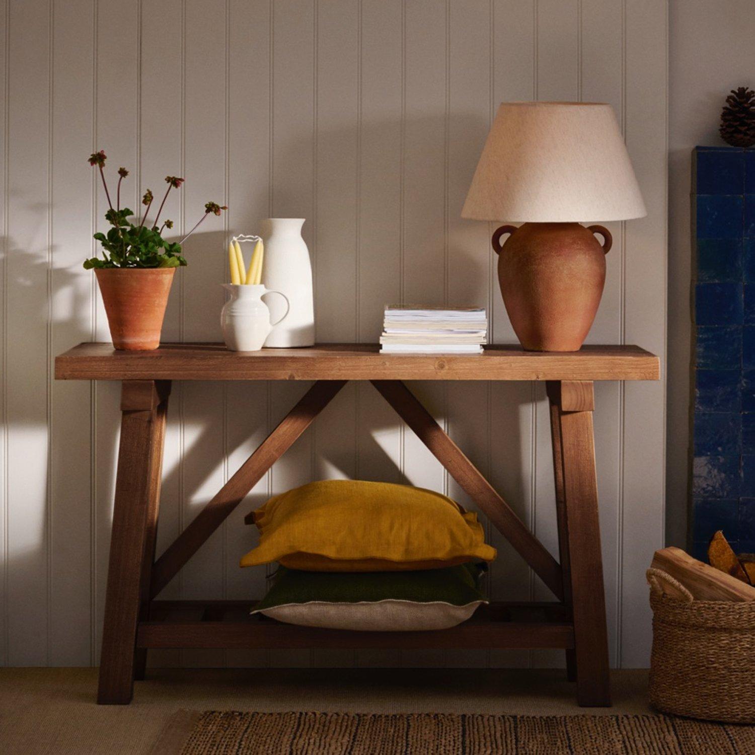 A side table with a plant pot, table lamp, magazines, and a few pots on display