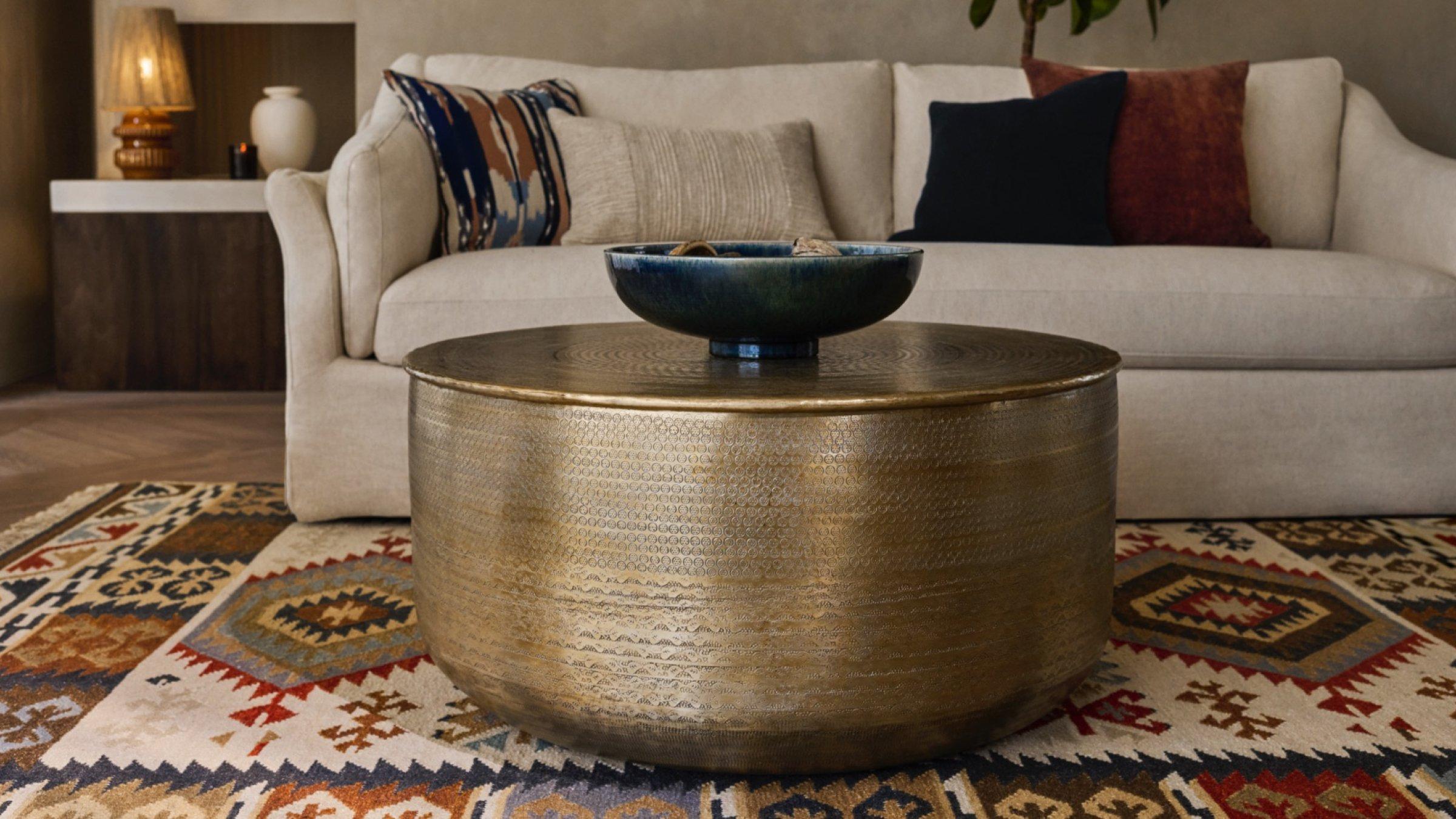 An antique brass coffee table, a white sofa with various patterned cushions, and other homeware accessories displayed in a lounge setting