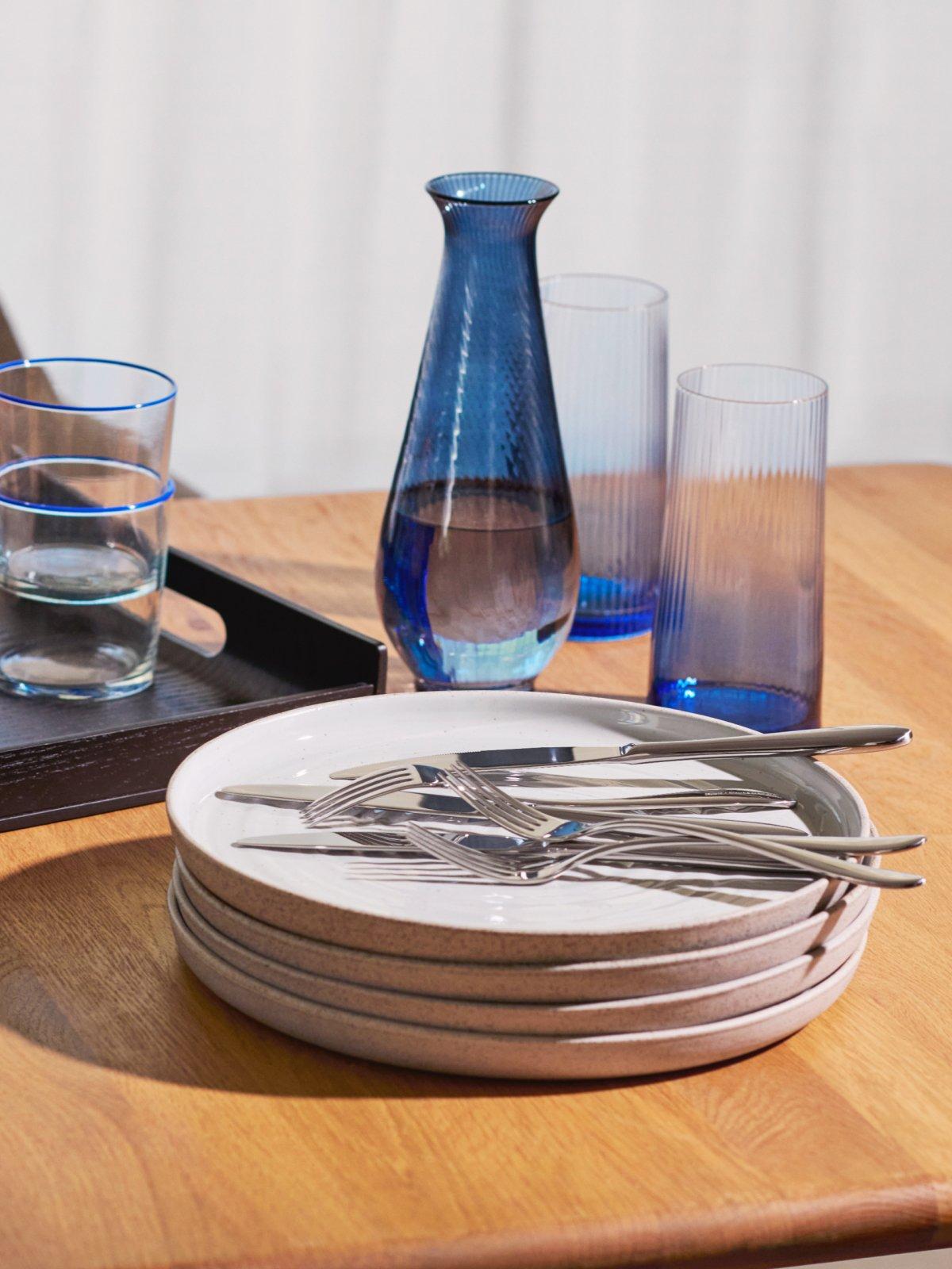 Scandi plate stack with forks and knives on top, a vase, and drinking glasses on a table