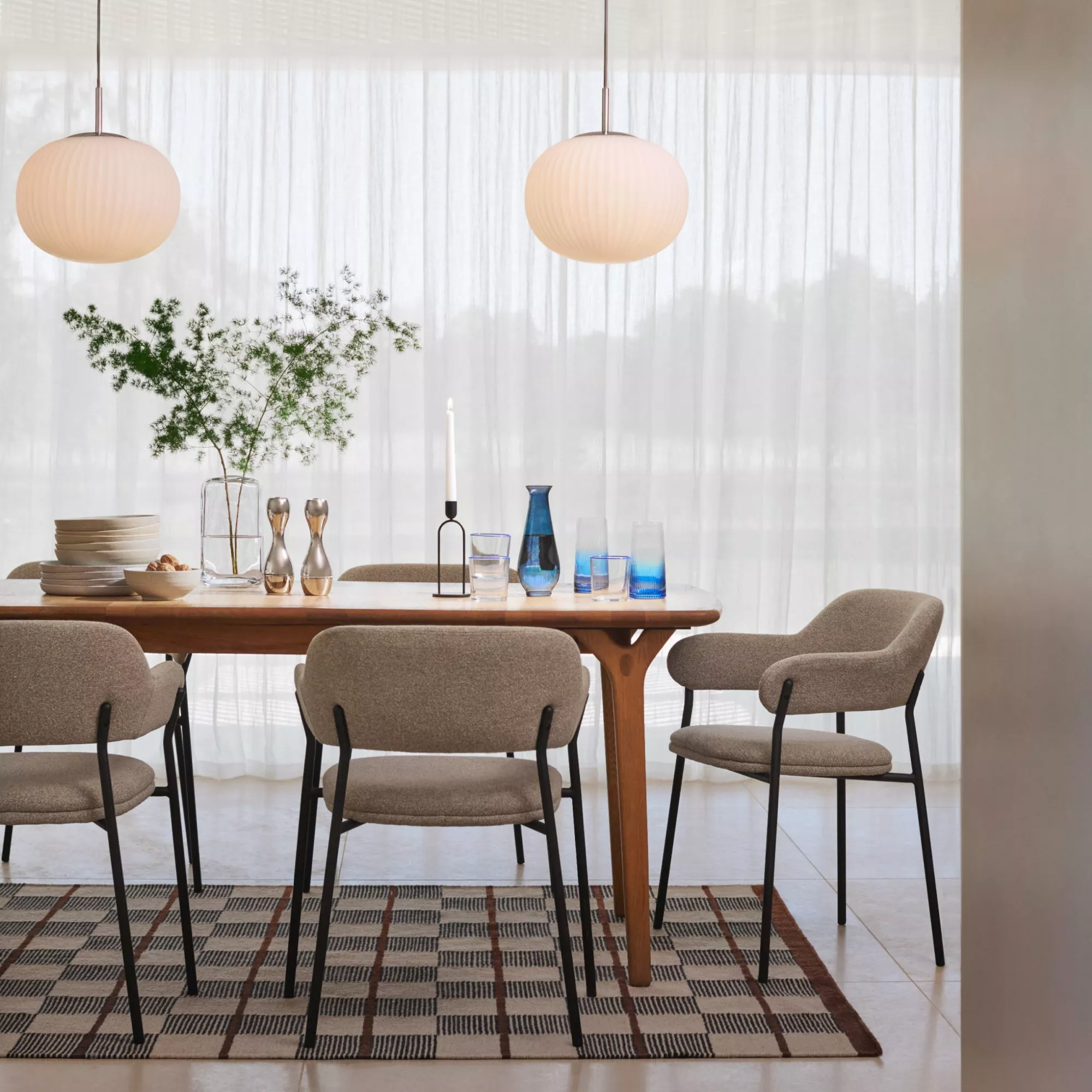 Minimalist style dining room with table chairs, geometric rug, round glass lampshades and soft opaque curtains