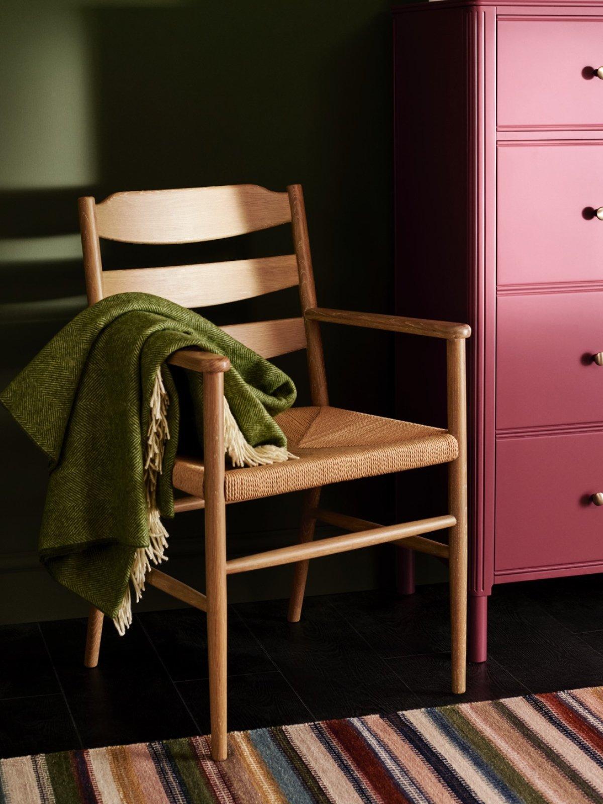 A green throw on a wooden chair, next to a bright pink chest of drawers