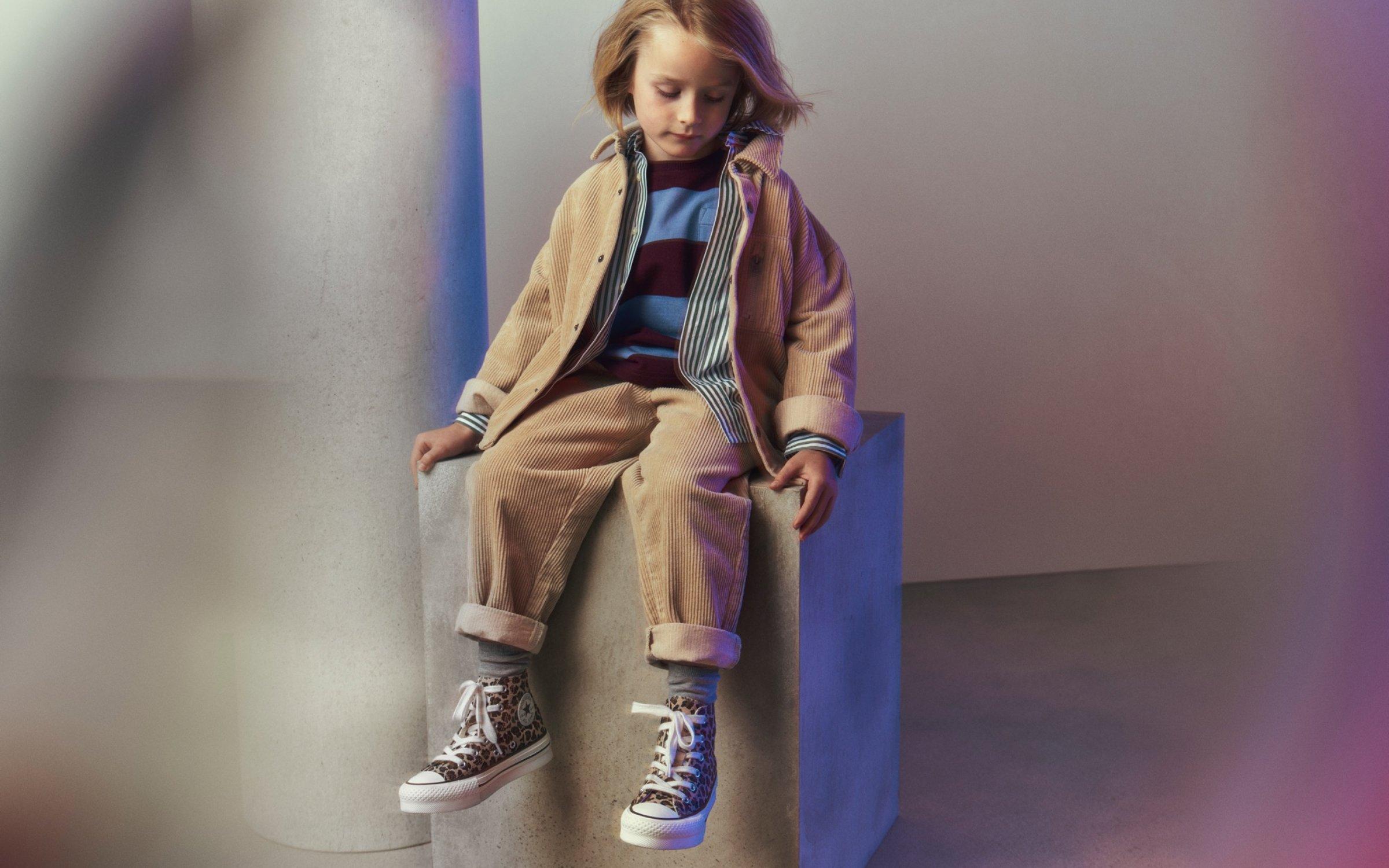 Boy sitting wearing a beige co-ord and Converse trainers