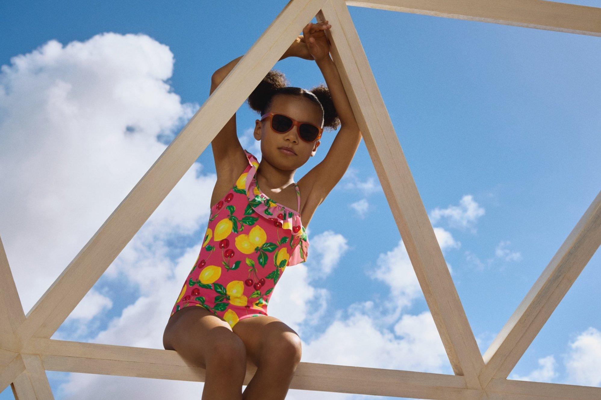 A girl wearing a red swimsuit is sitting on a wooden play structure