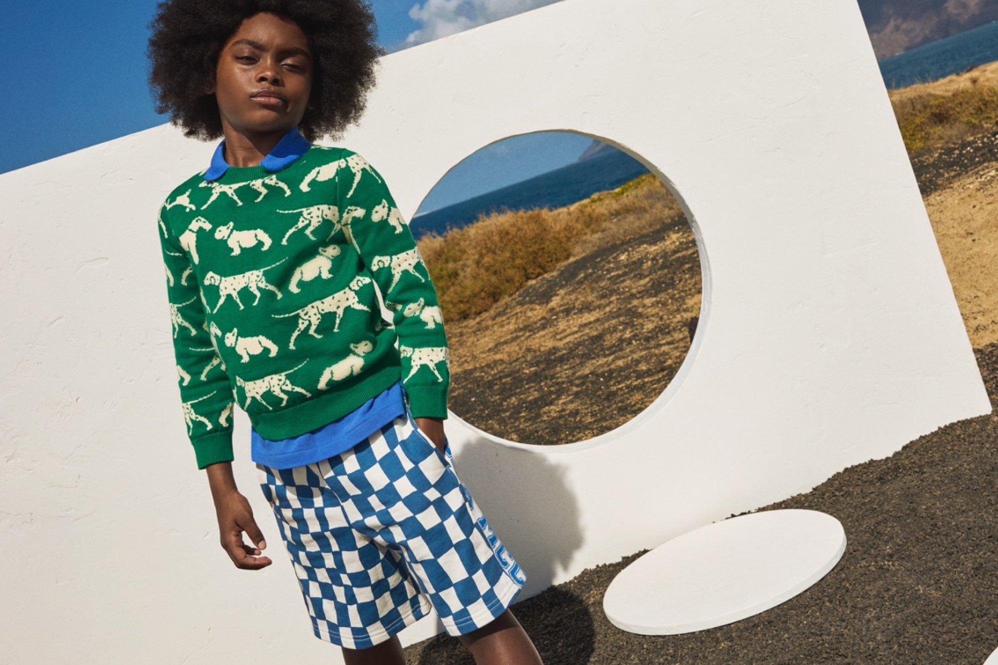 A boy posing outside wearing a animal-patterned green top and blue checkered shorts